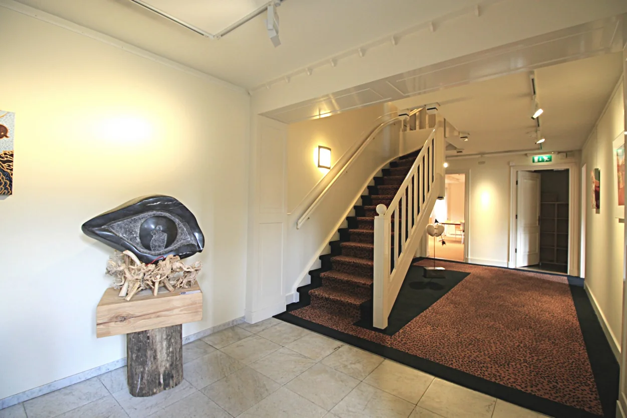 Ingang van een modern museum aan de Museumlaan met een trap, kunstwerken aan de muur en een sculptuur op een sokkel.