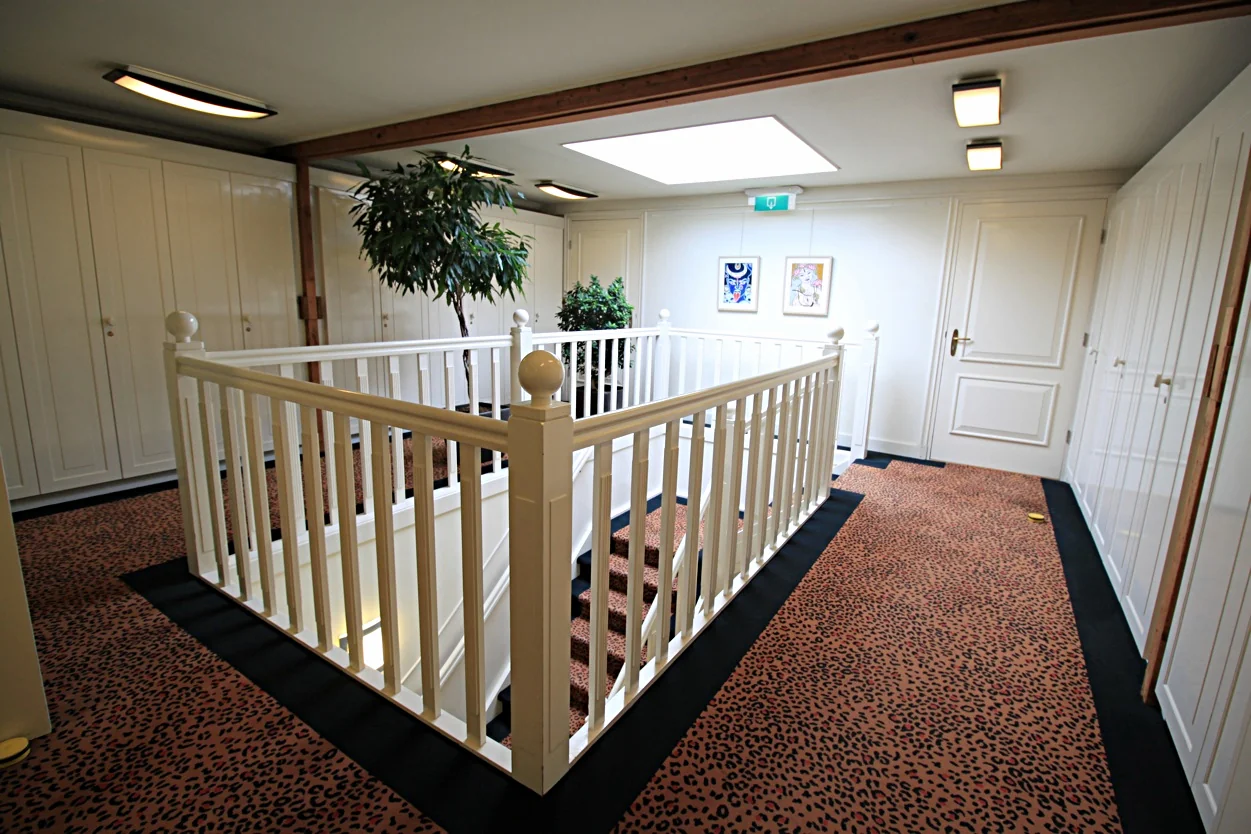 Bovenverdieping van een woning aan de Museumlaan met een trapgat, luipaardprint tapijt, witte deuren en sierplanten.