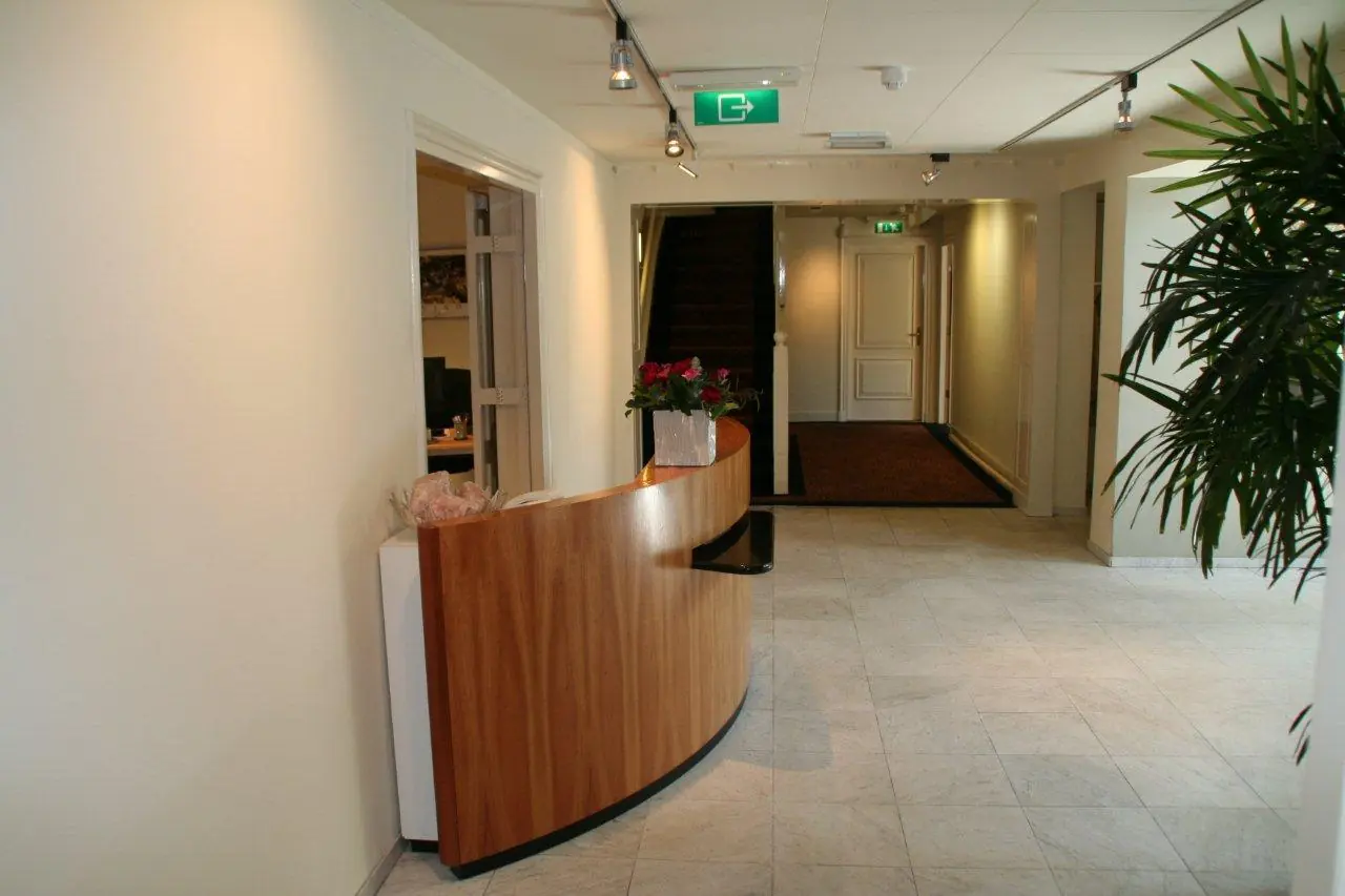 Receptiebalie in een lichte hal aan de Museumlaan met een trap en deuren op de achtergrond.