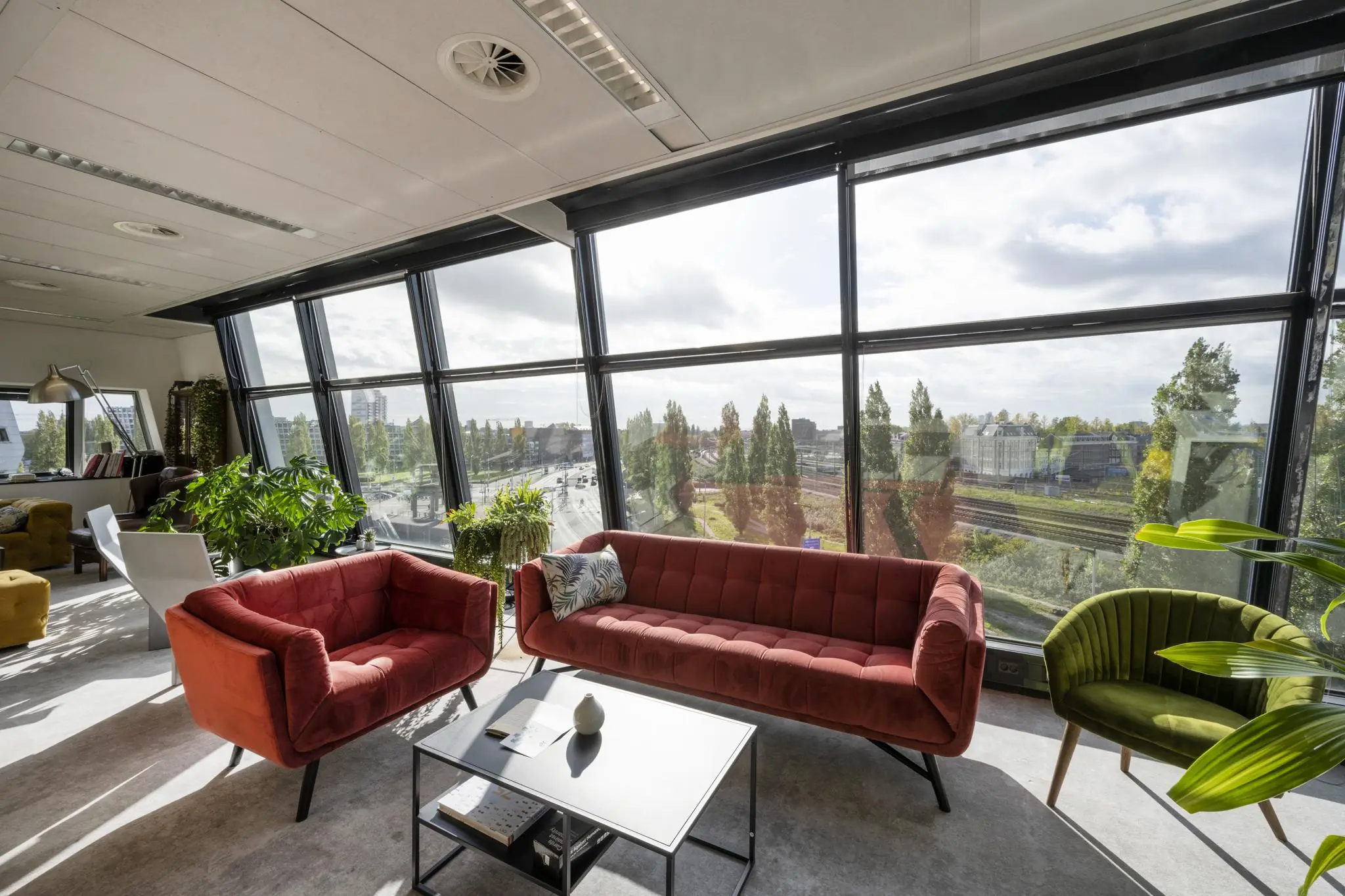 Lichte en moderne loungehoek met kleurrijke zitmeubels en uitzicht op het Rietlandpark via grote panoramavensters.