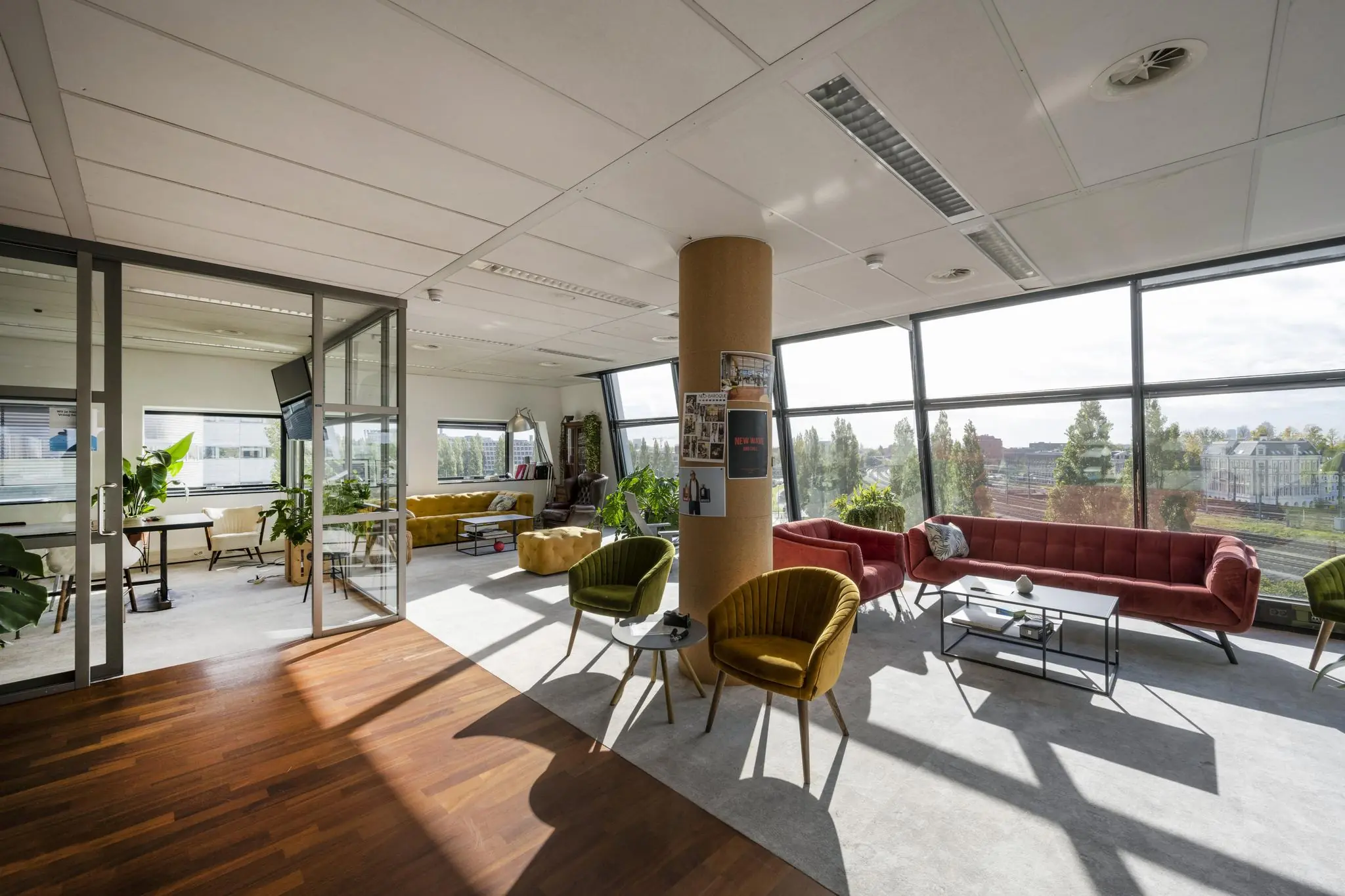 Moderne en licht ingerichte kantoorlounge in Rietlandpark met kleurrijke zitmeubels en grote ramen met uitzicht op het spoor en omliggende gebouwen.