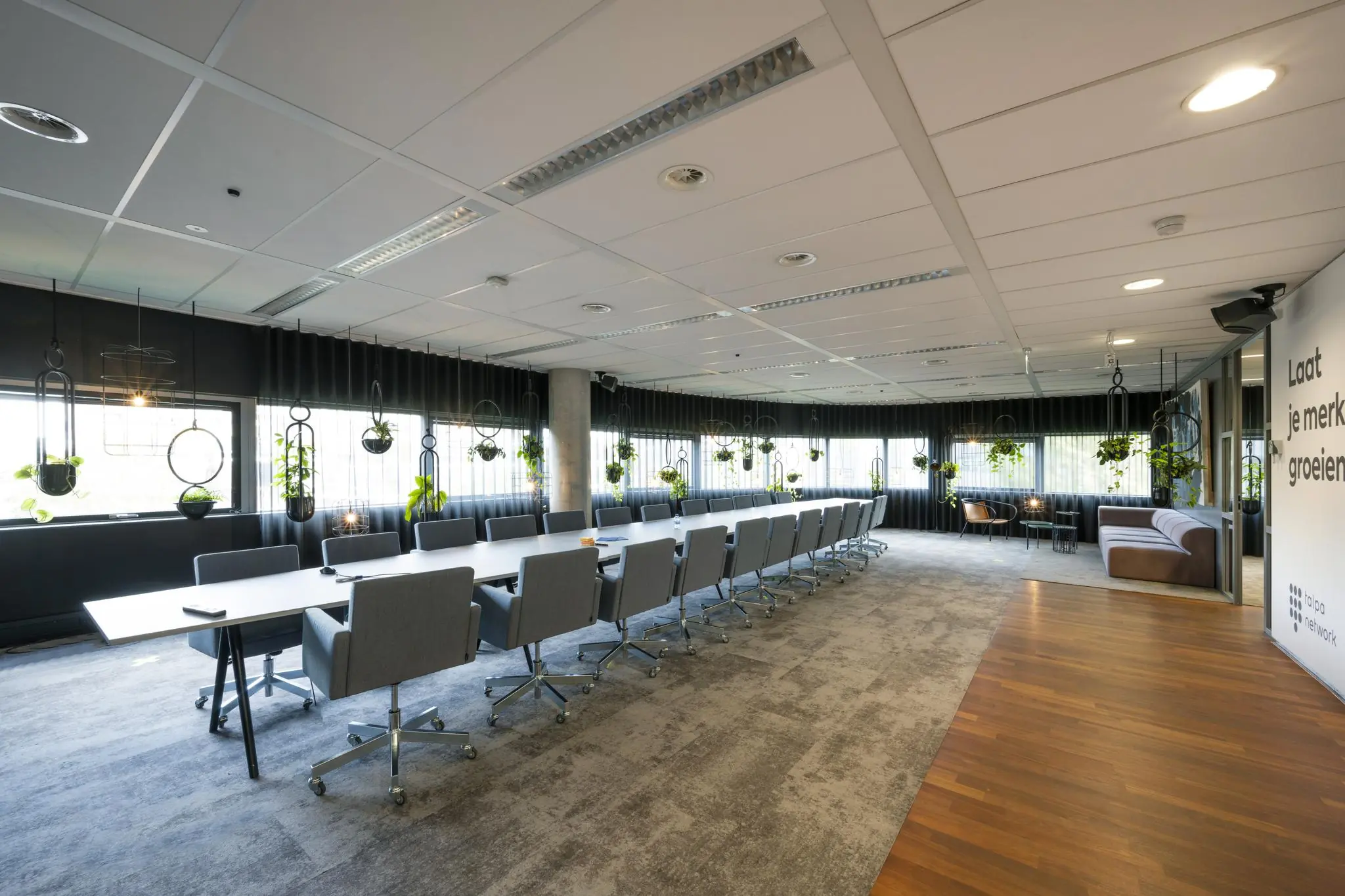 Moderne vergaderruimte in Rietlandpark met lange tafel, grijze stoelen en hangplanten bij de ramen.