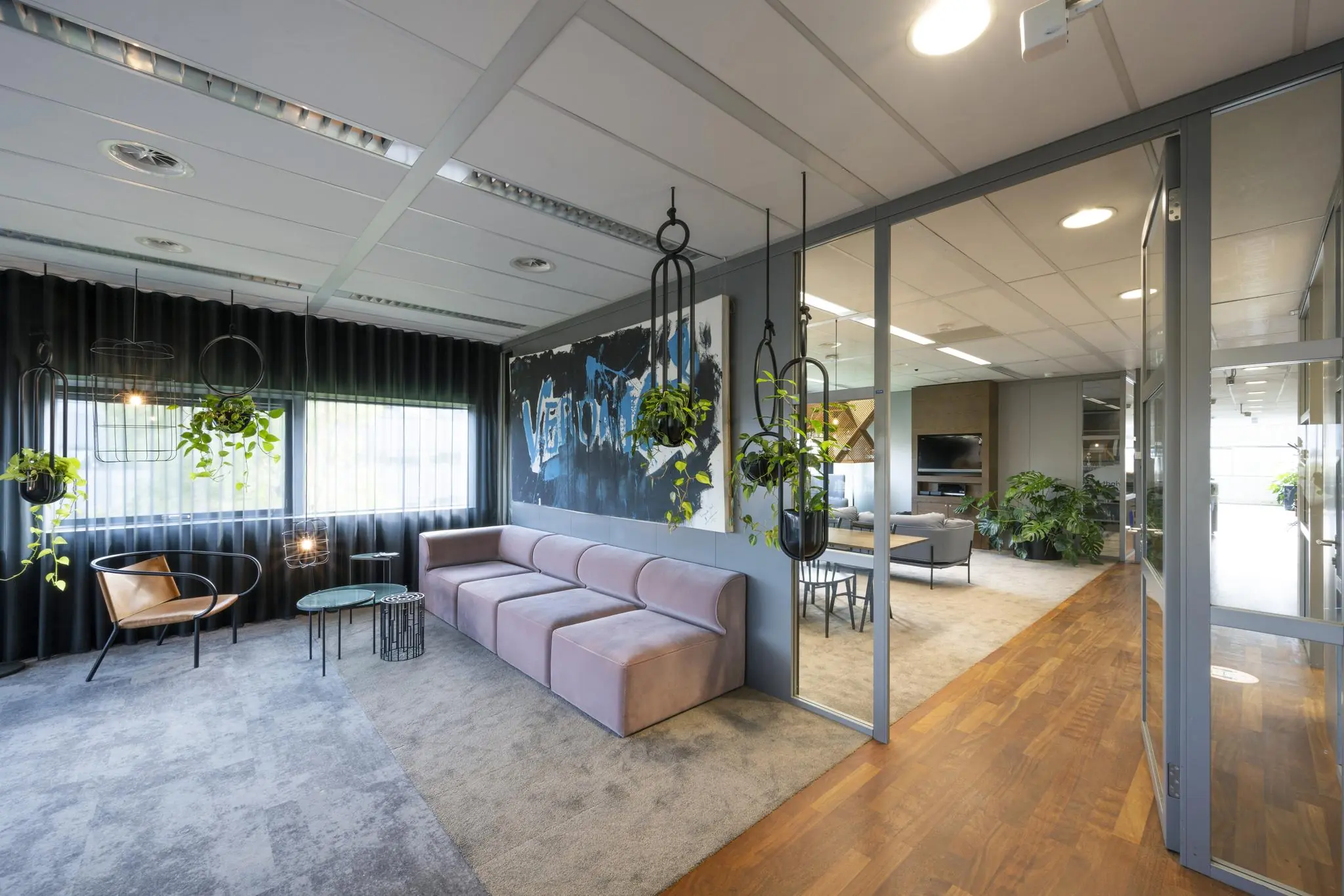 Moderne kantoorlounge in Rietlandpark met pastelroze bank, hangplanten en glazen wanden.