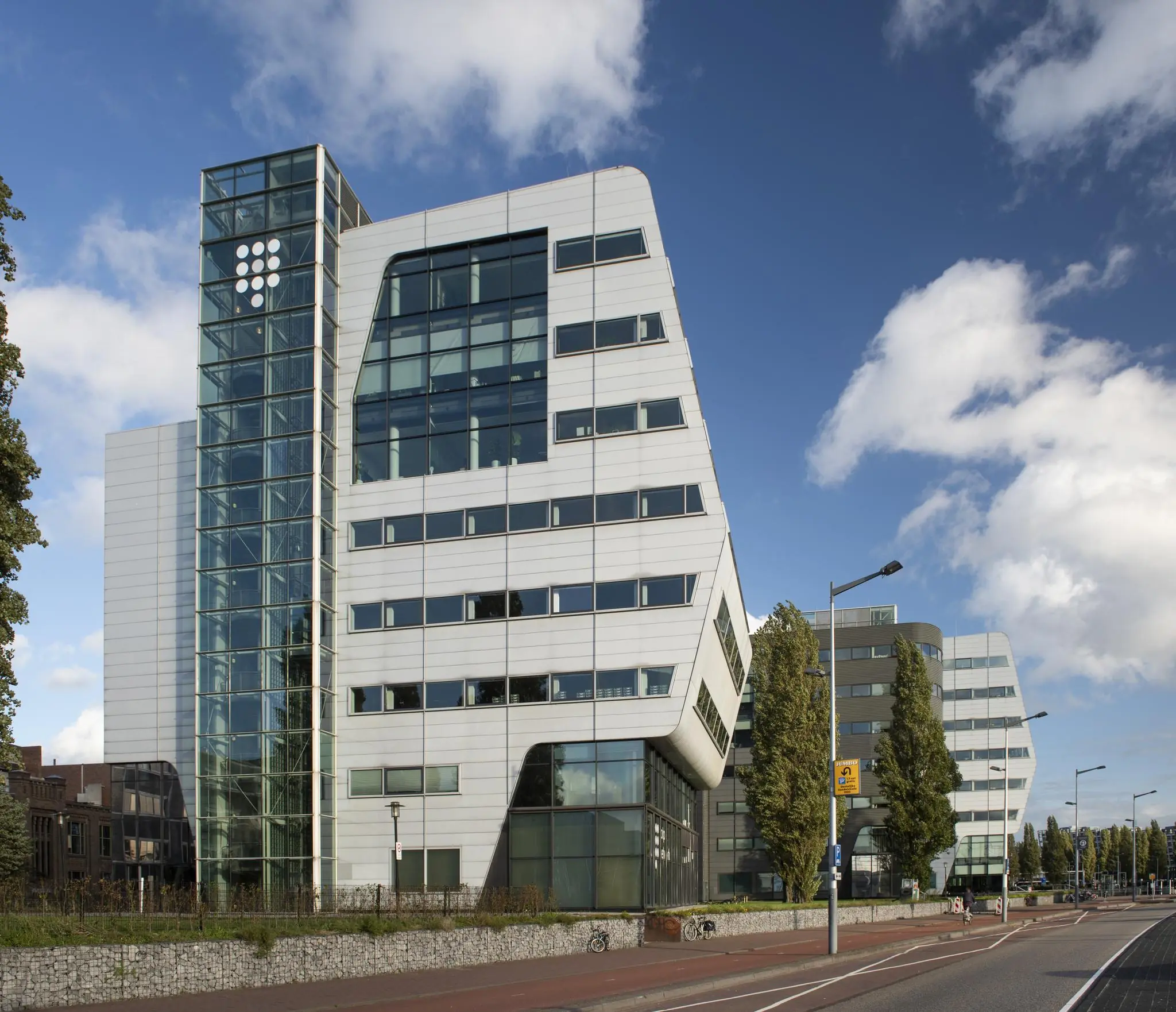 Modern kantoorgebouw Rietlandpark in Amsterdam met witte gevelpanelen en schuine vormen langs een brede weg.