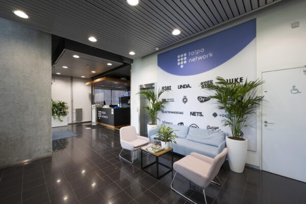 Moderne wachtruimte bij Talpa Network met zitbank, stoelen, planten en een wand met logo’s van mediakanalen.
