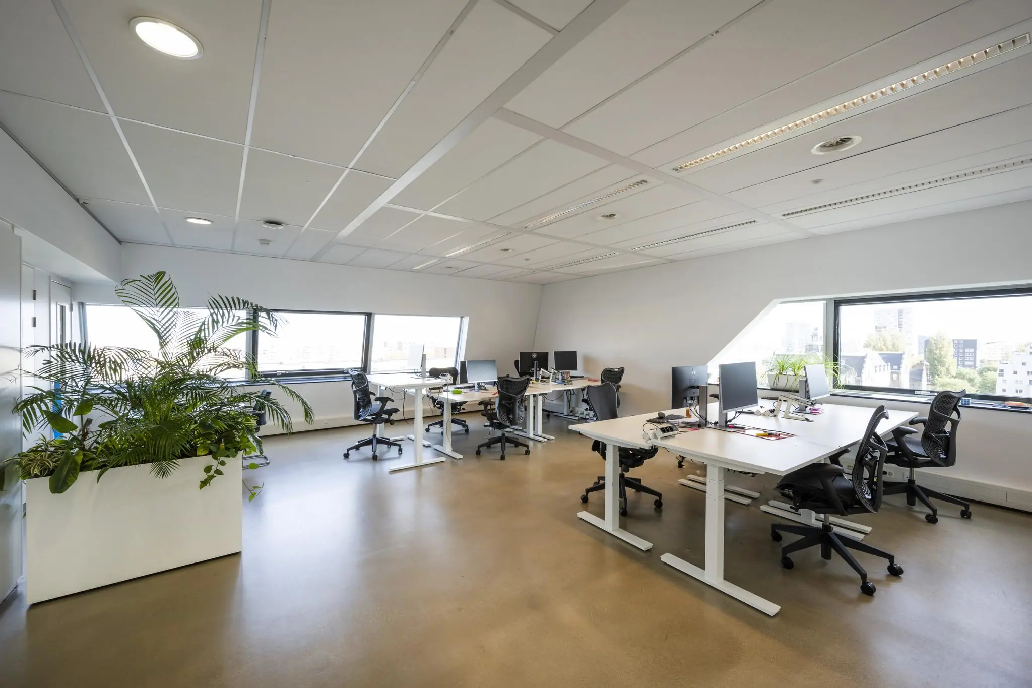 Modern kantoorinterieur in Rietlandpark met meerdere werkplekken, bureaustoelen, computers en grote ramen met uitzicht op de stad.