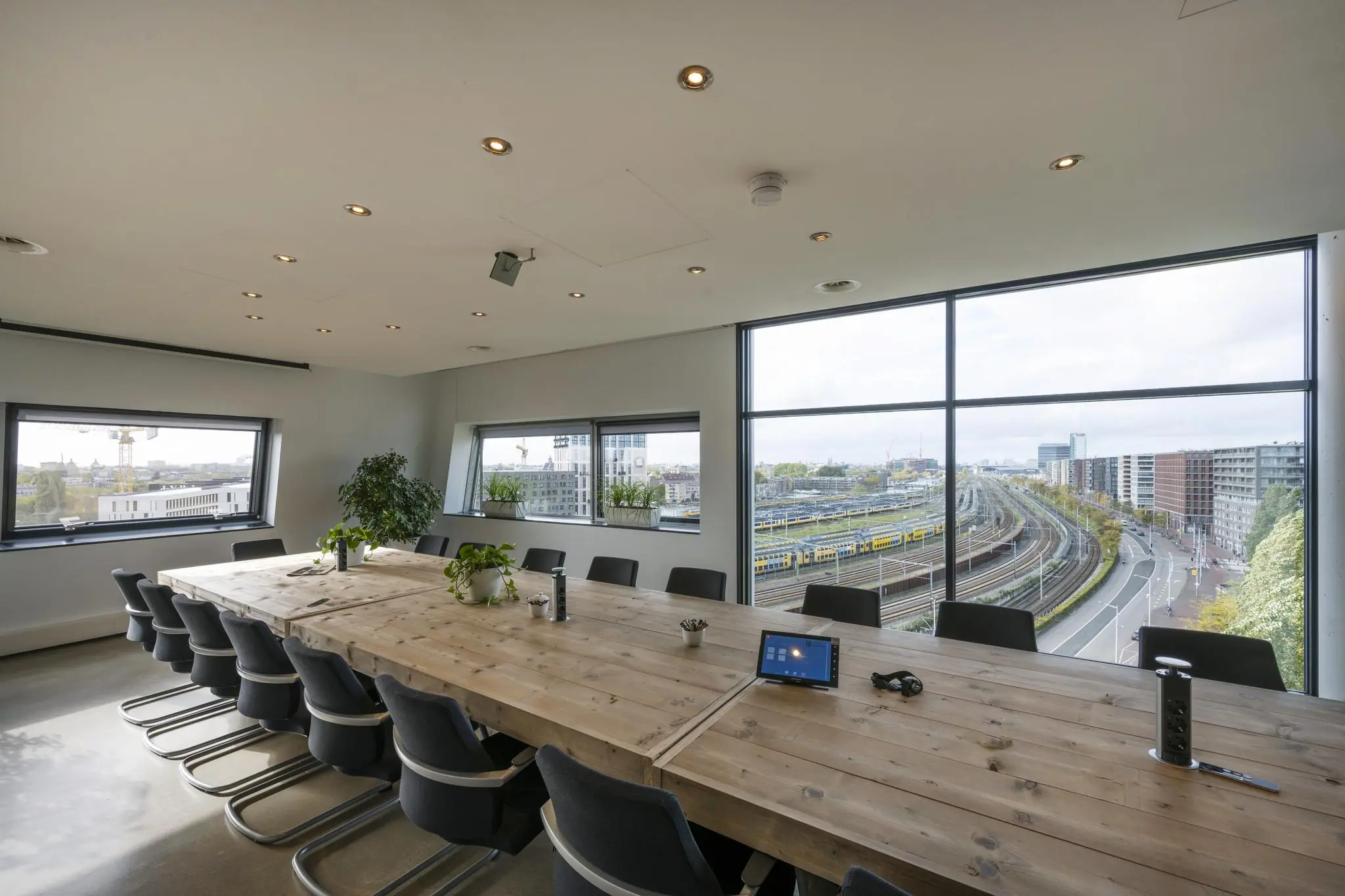 Vergaderruimte met houten tafel en uitzicht op spoorlijnen en moderne gebouwen in Rietlandpark, Amsterdam.