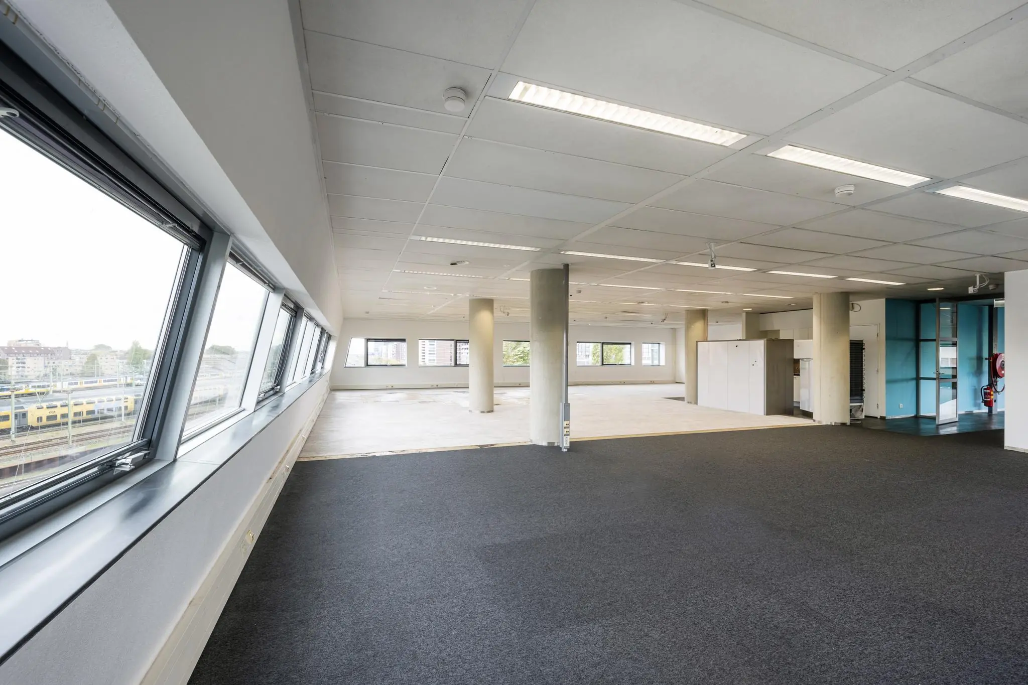 Lichte, lege kantoorruimte aan het Rietlandpark met grote ramen en uitzicht op een spoorlijn.