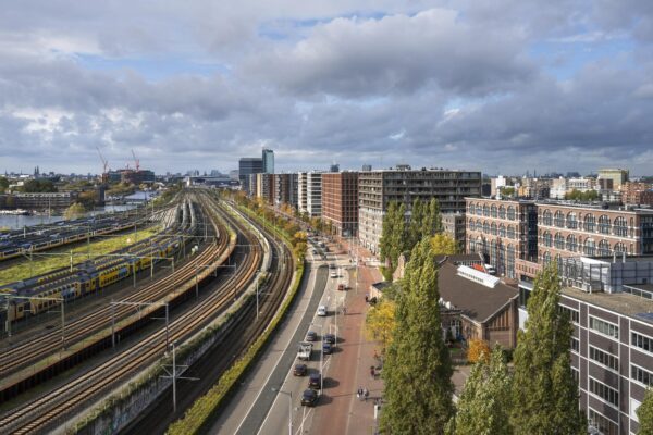 Luchtfoto van Rietlandpark in Amsterdam met treinsporen, woongebouwen en een drukke stadsweg.