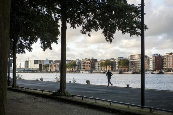 Jogger rent langs het water met uitzicht op de moderne woongebouwen van Rietlandpark in Amsterdam.