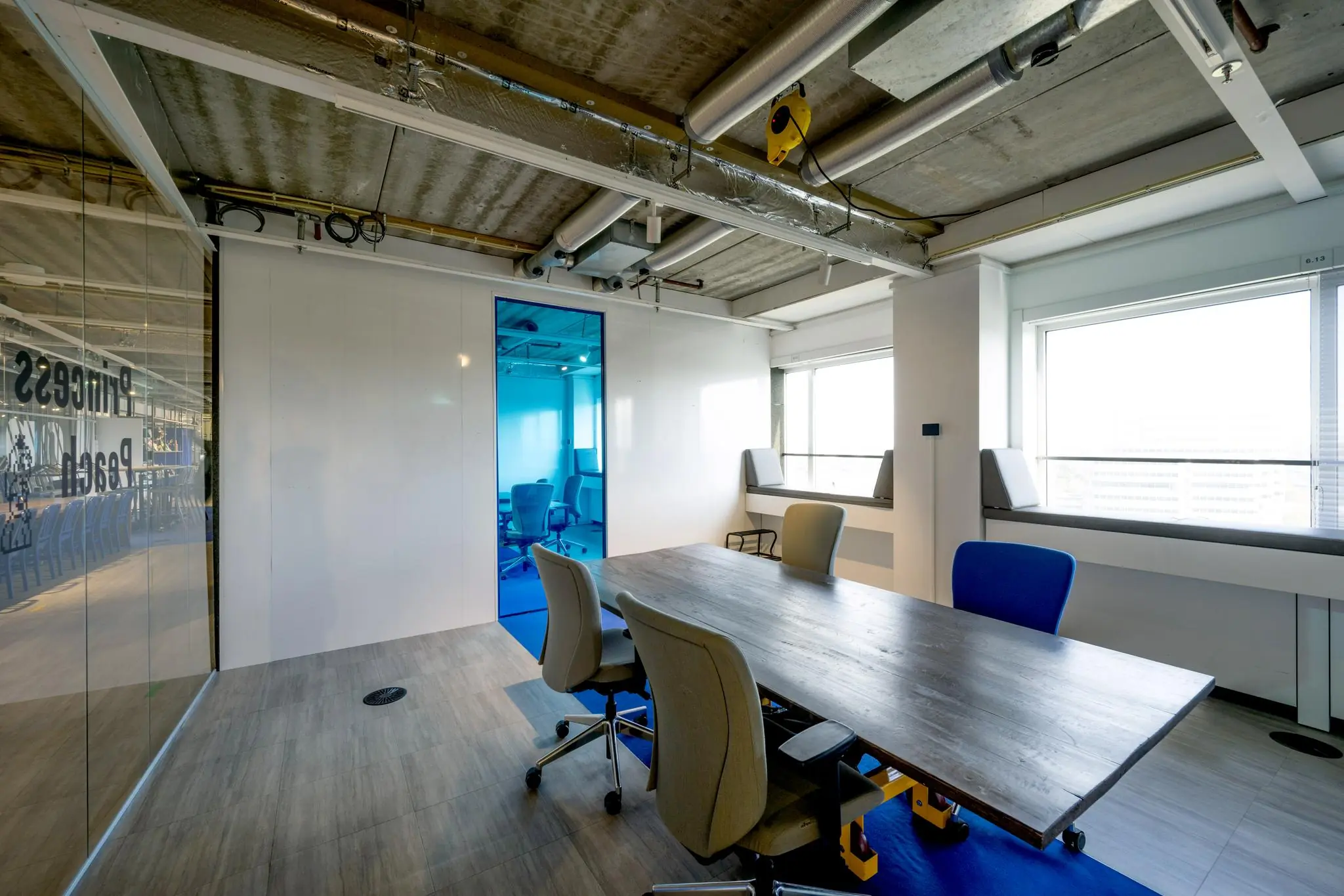 Vergaderruimte met moderne inrichting in een kantoor aan de Johan Huizingalaan, met zicht op een blauwe vergaderruimte en grote ramen.