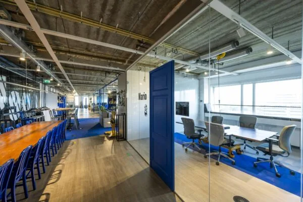 Modern kantoorinterieur aan de Johan Huizingalaan met glazen vergaderruimte genaamd "Mario" en een lange houten vergadertafel.