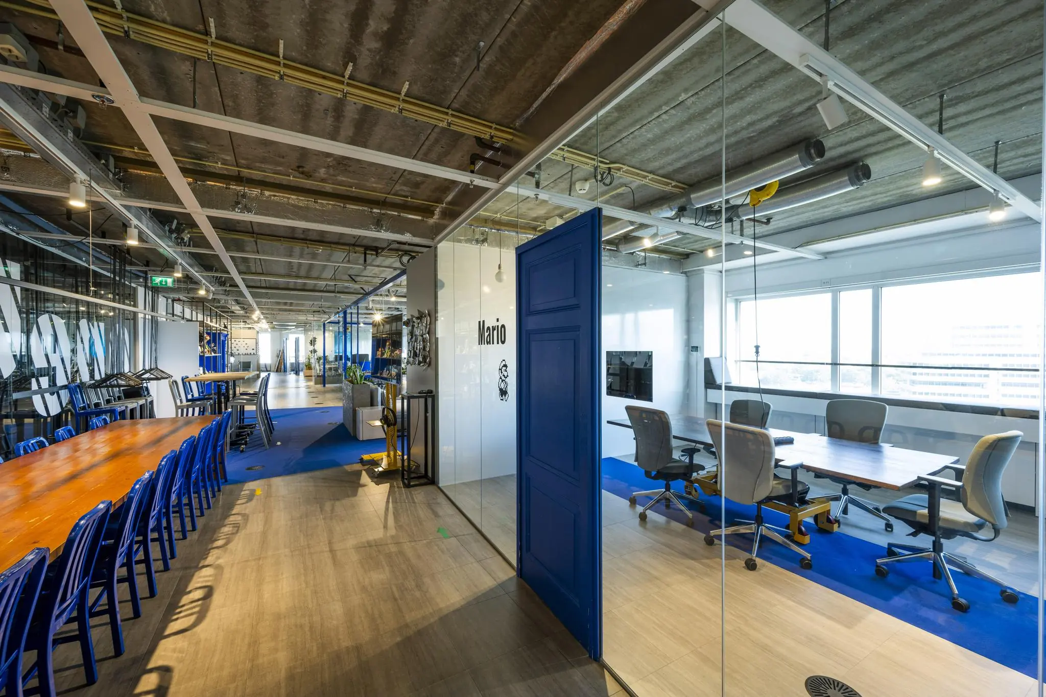 Modern kantoorinterieur aan de Johan Huizingalaan met glazen vergaderruimte genaamd "Mario" en een lange houten vergadertafel.