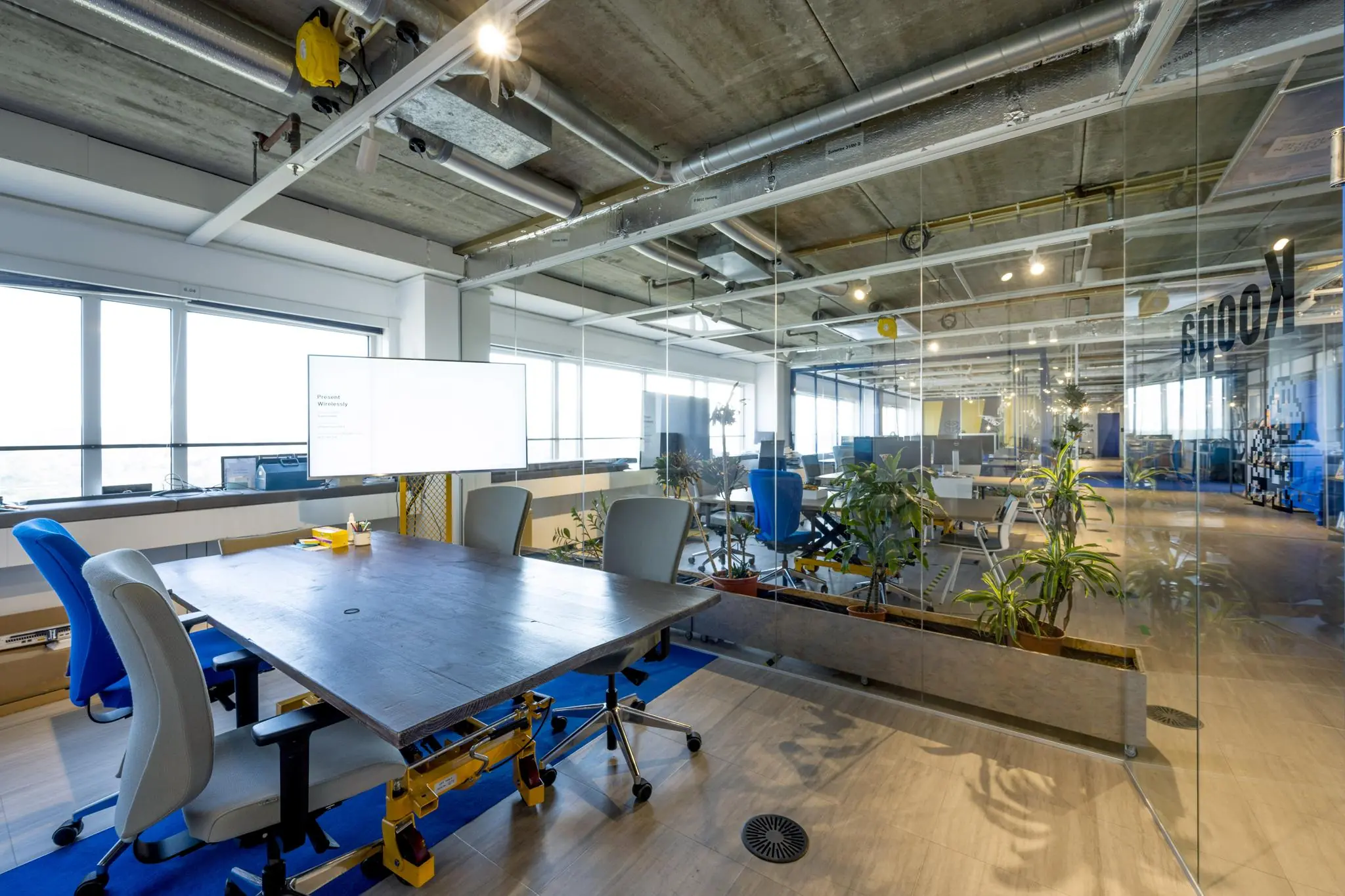 Moderne kantoorruimte aan de Johan Huizingalaan met vergadertafel, bureaustoelen en glazen wanden met zicht op open werkplekken en planten.