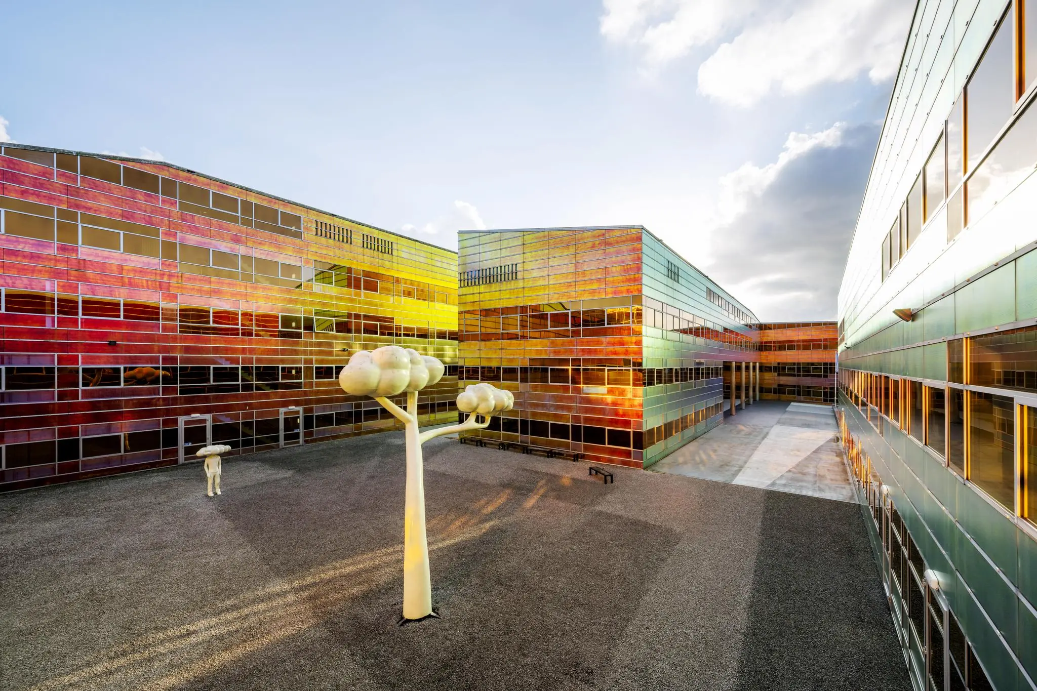 Binnenplaats van het kleurrijke gebouw aan de W. Dreesweg met glanzende gevelpanelen en kunstzinnige boomsculpturen.