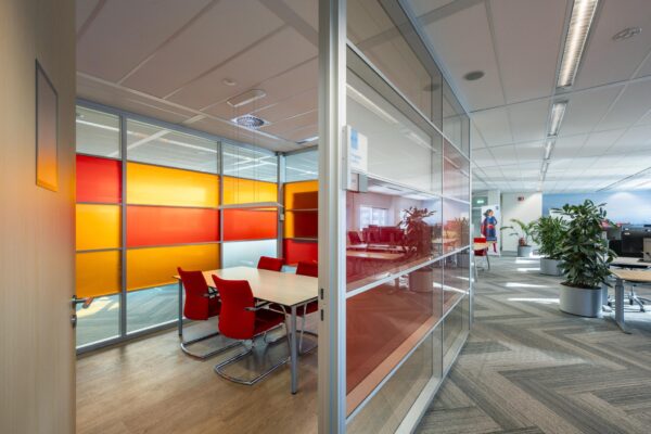 Moderne kantoorruimte aan de W. Dreesweg met een vergaderruimte met gekleurde glaswanden en rode stoelen.