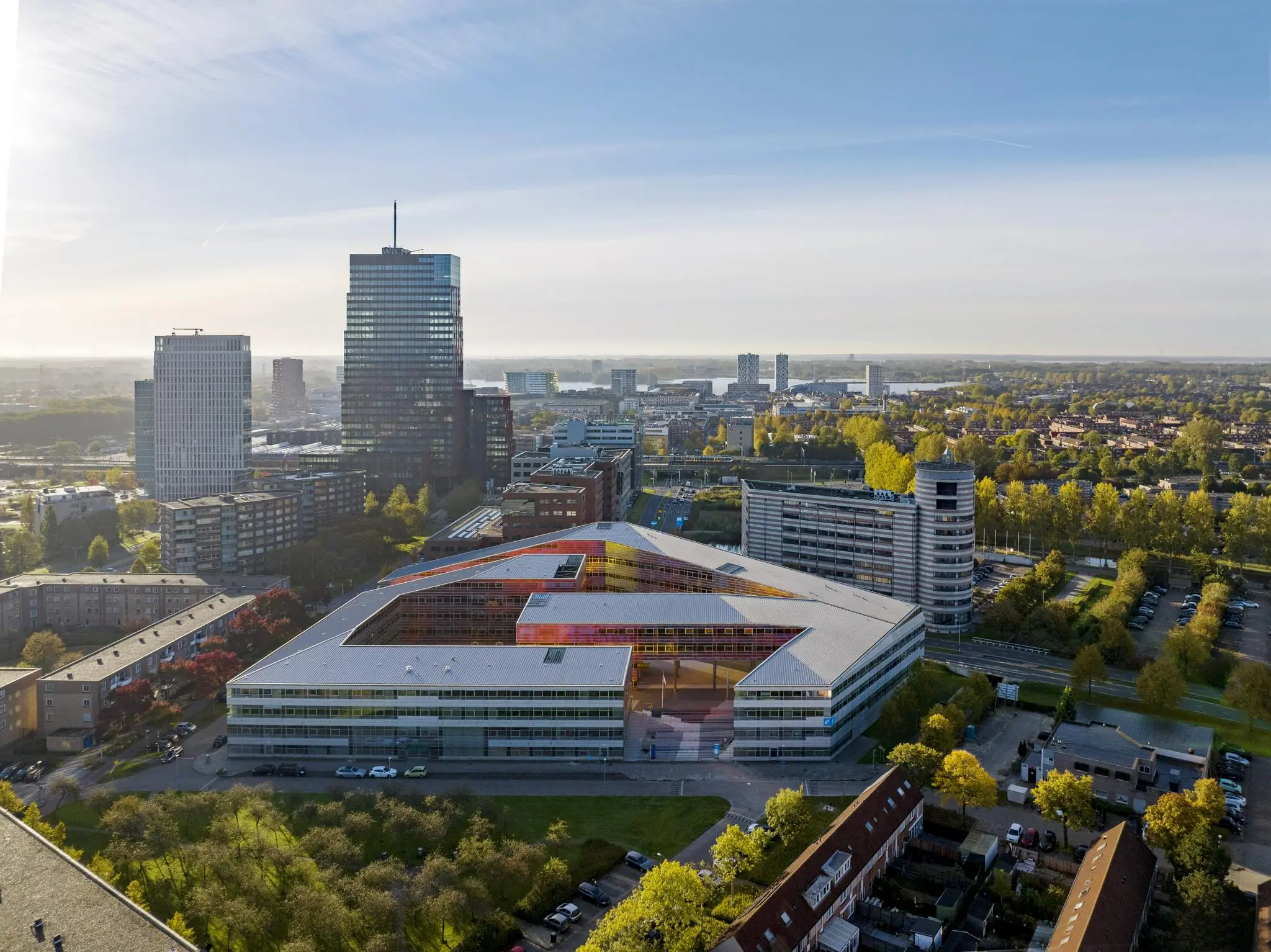 Luchtfoto van het kleurrijke scholencomplex aan de W. Dreesweg in Amstelveen, omringd door hoge kantoorgebouwen en woonwijken.