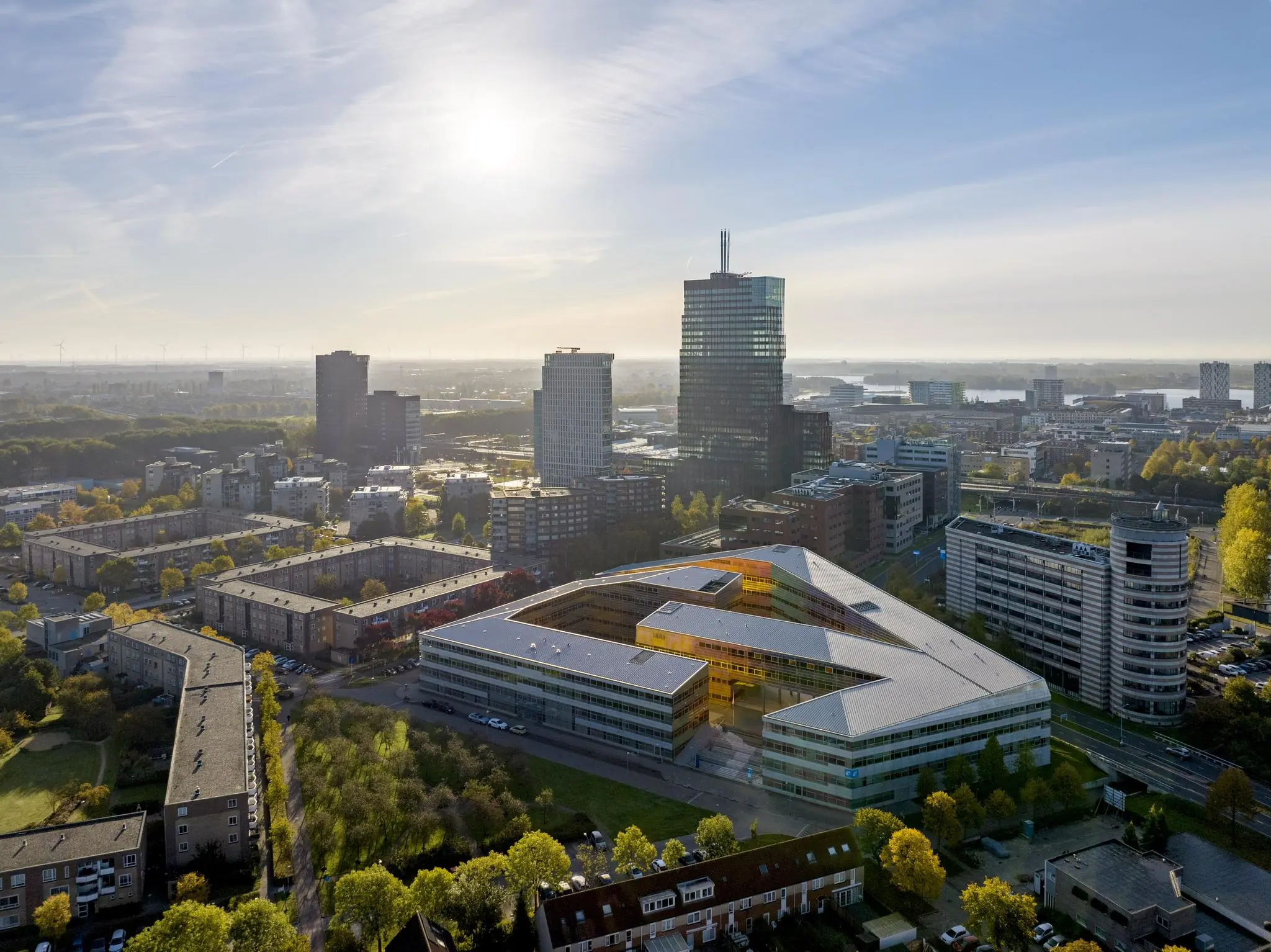 Luchtfoto van het moderne gebouw aan de W. Dreesweg in een stedelijk gebied met hoge kantoortorens en omliggende woonwijken.