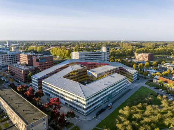 Luchtfoto van het opvallend gekleurde kantoorgebouw aan de Mr. W. Dreesweg in Amstelveen, omringd door bomen en andere zakelijke panden.
