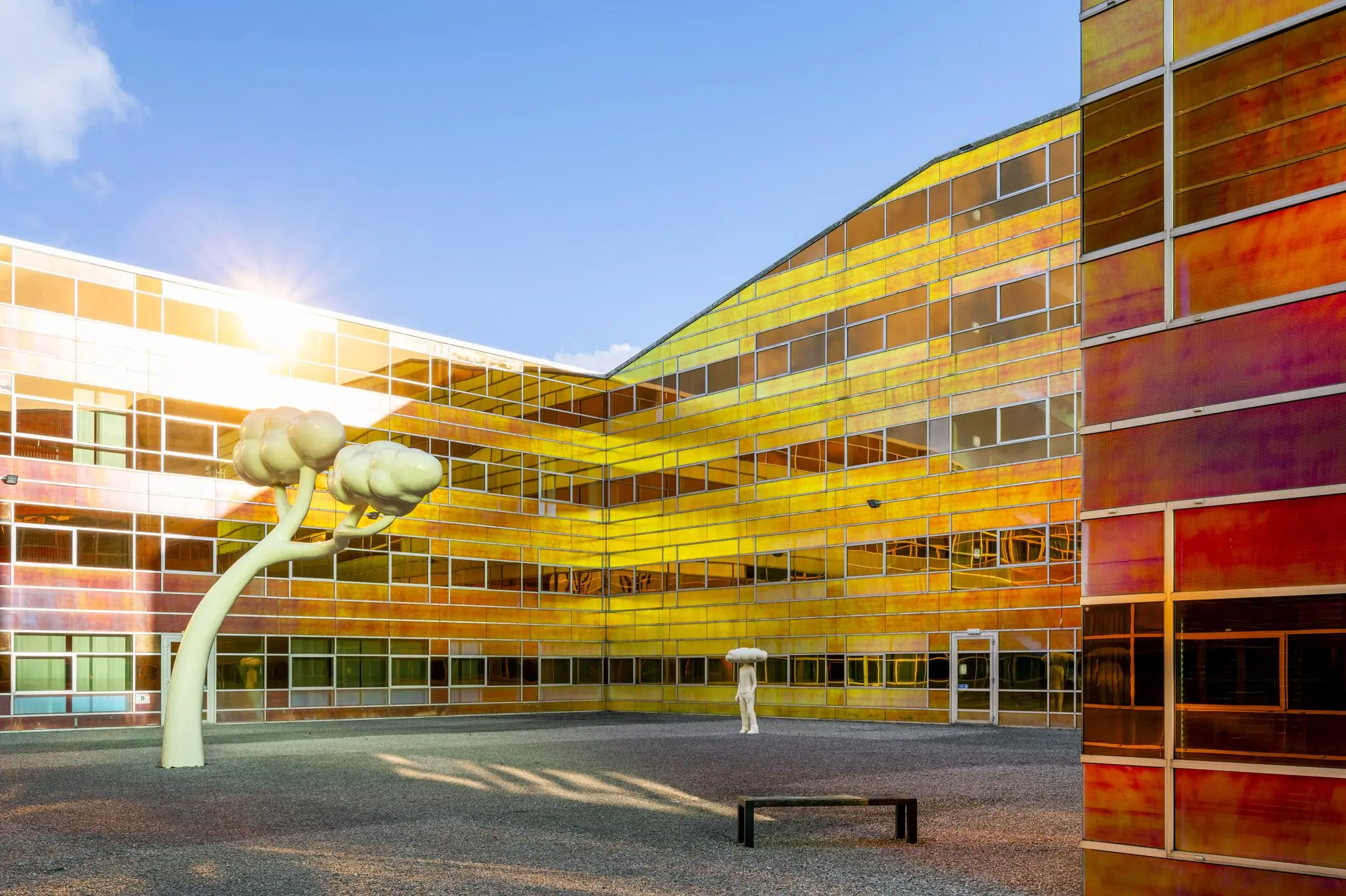 Binnenplaats van een modern gebouw aan de W. Dreesweg met kleurrijke, reflecterende gevelpanelen en opvallende kunstobjecten.