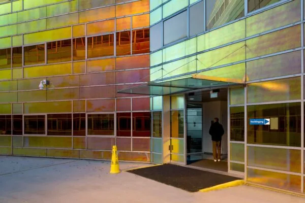 Hoofdingang van een modern gebouw aan de W. Dreesweg met gekleurde glazen gevel en een persoon die naar binnen loopt.