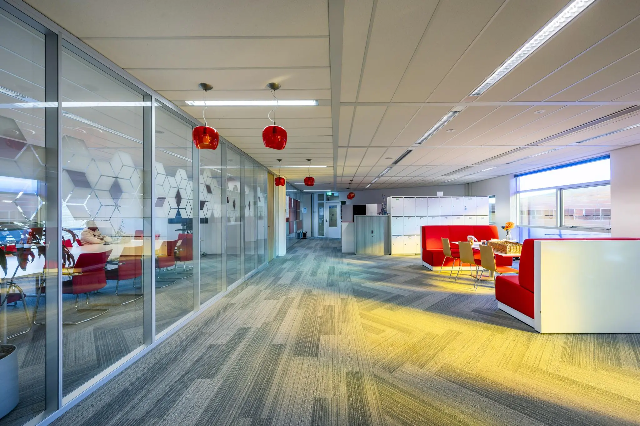 Moderne kantoorruimte aan de W. Dreesweg met glazen vergaderruimtes, rode accenten en een zithoek met lockers.