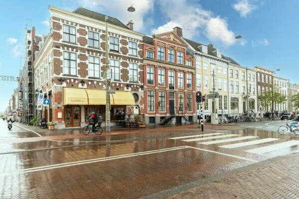 Straatbeeld van de Prinsestraat en de Prinsengracht in Den Haag met karakteristieke gevels, fietsers en een regenachtig wegdek.