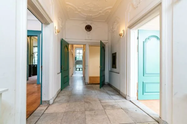 Monumentale gang met hoge plafonds, sierlijke ornamenten en openstaande turquoise deuren aan de Prinsegracht.