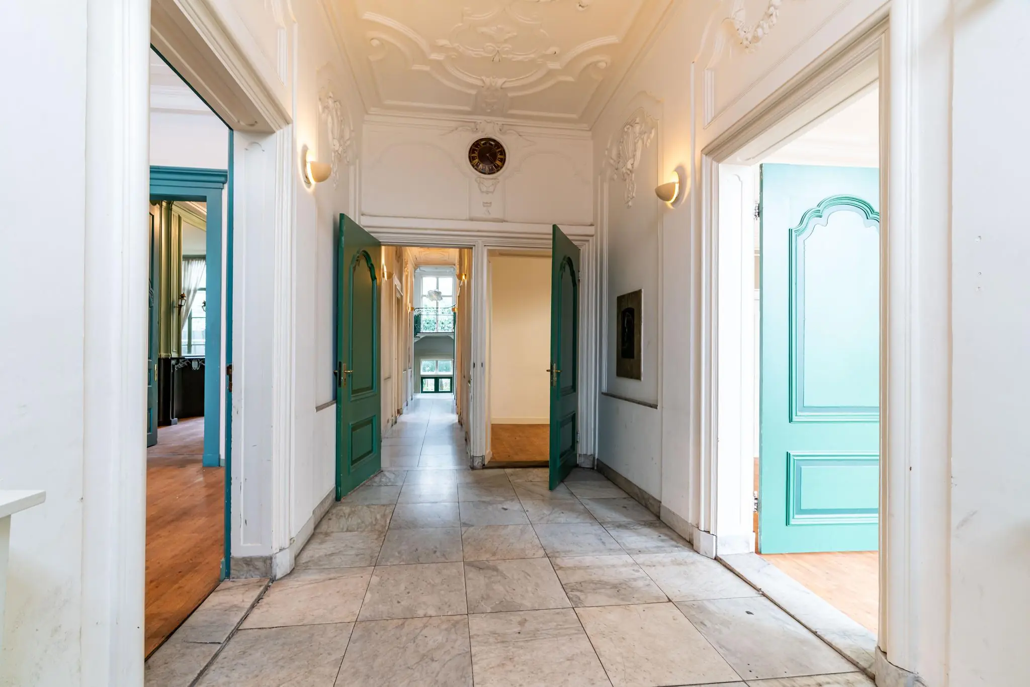 Monumentale gang met hoge plafonds, sierlijke ornamenten en openstaande turquoise deuren aan de Prinsegracht.