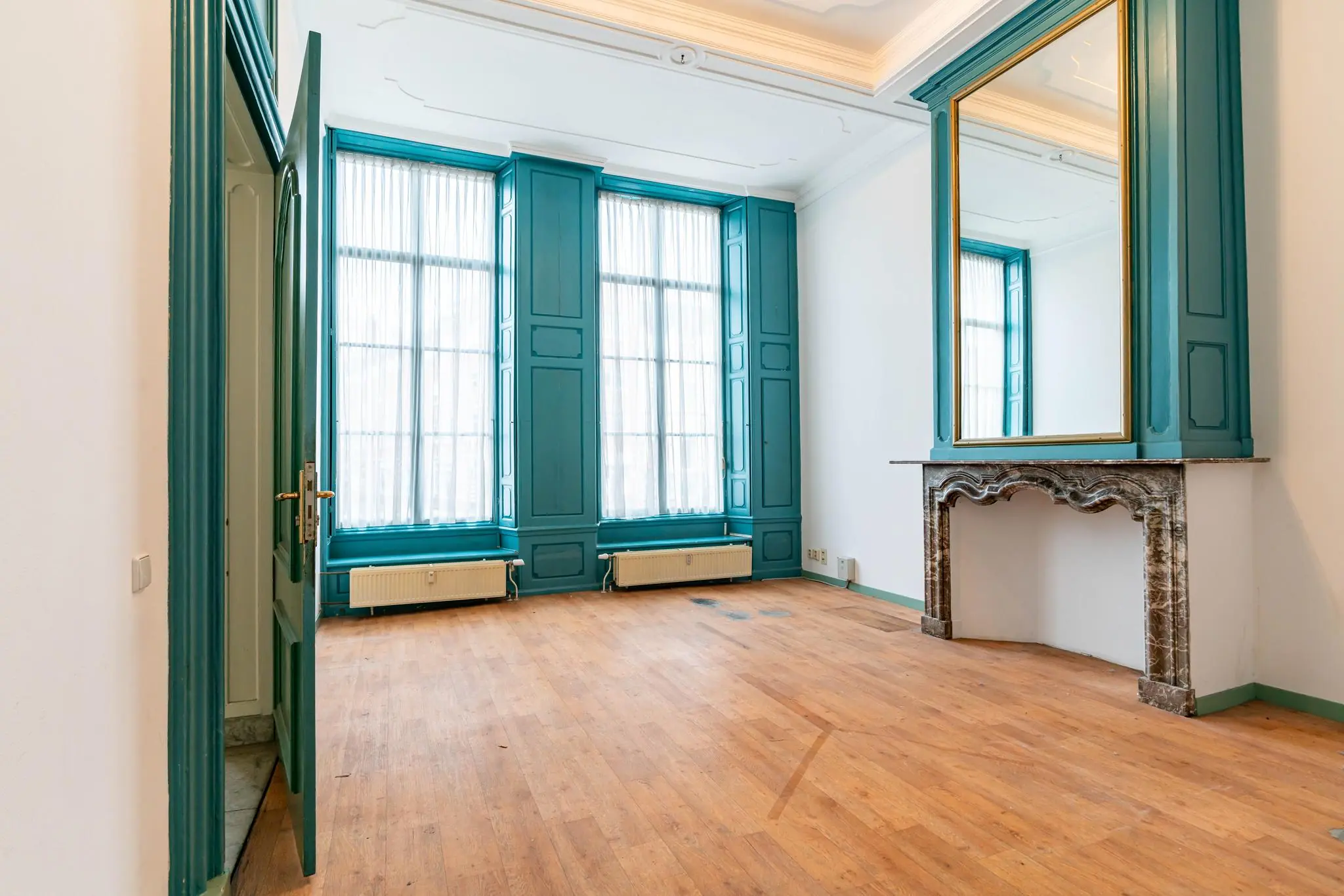 Lichte kamer aan de Prinsegracht met houten vloer, sierhaard en hoge ramen met turquoise kozijnen.