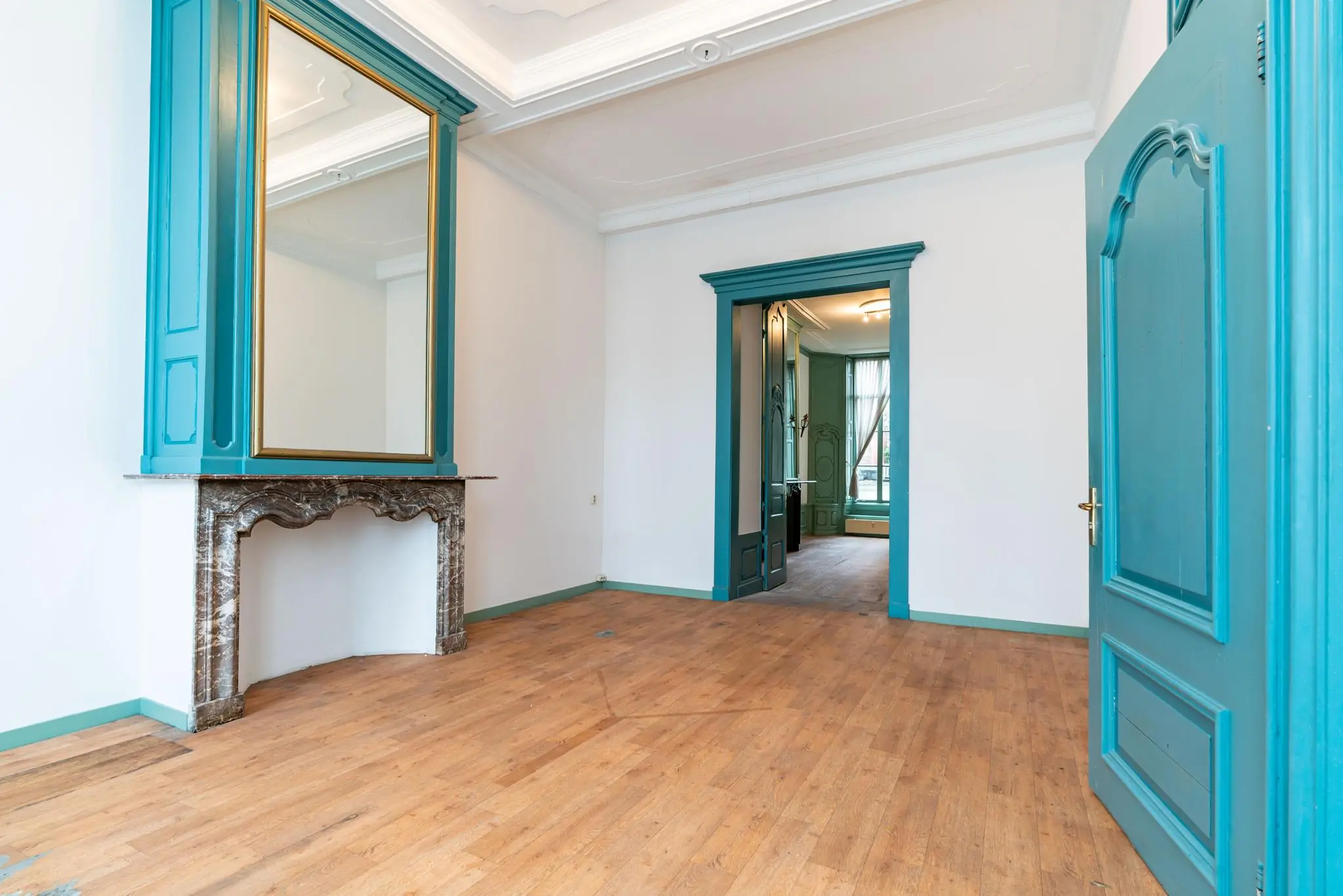 Stijlvolle kamer aan de Prinsegracht met houten vloer, hoge plafonds en turquoise accenten rond deuren en schouw.