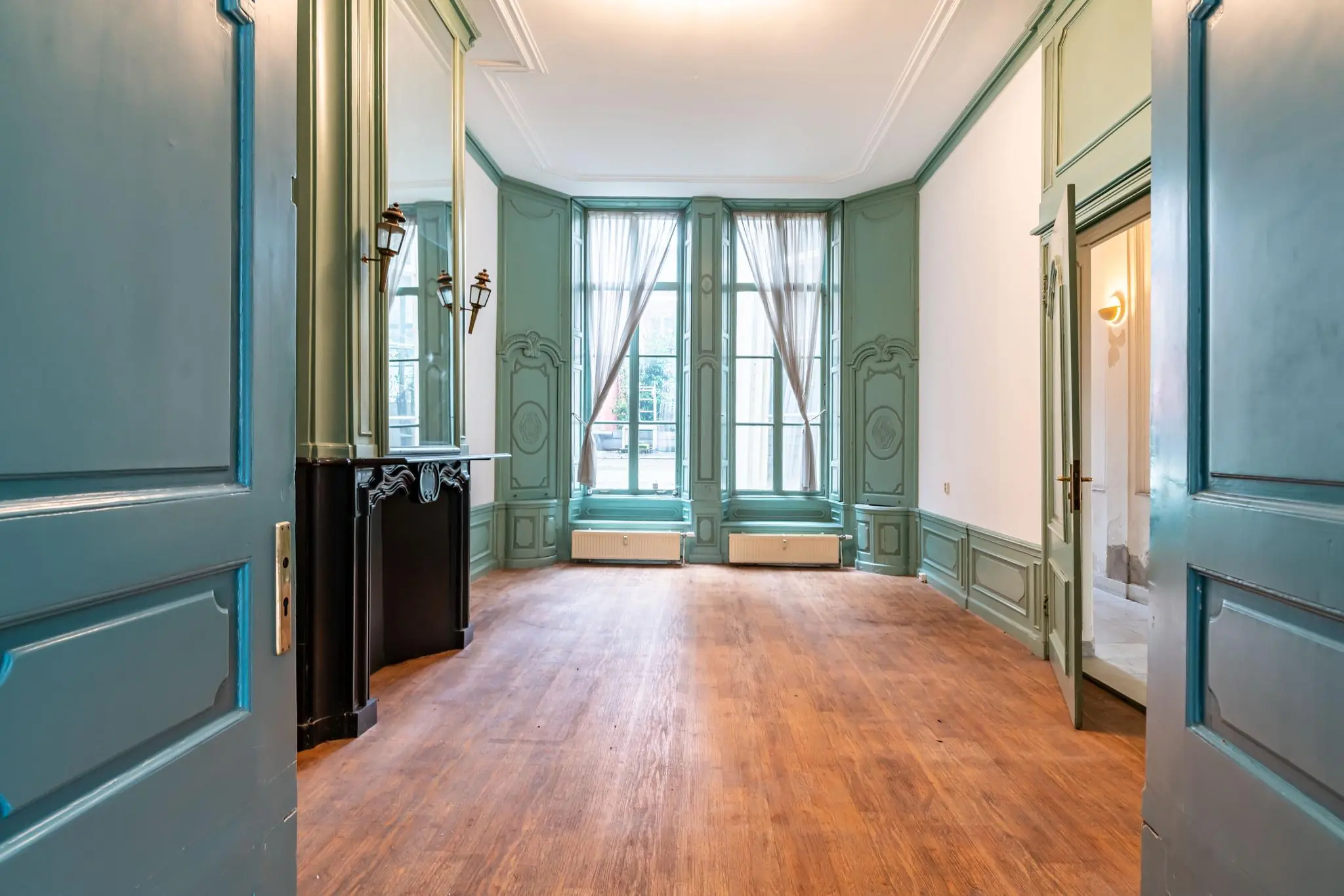 Klassieke kamer aan de Prinsegracht met hoge ramen, houten vloer en groenblauwe wandpanelen.