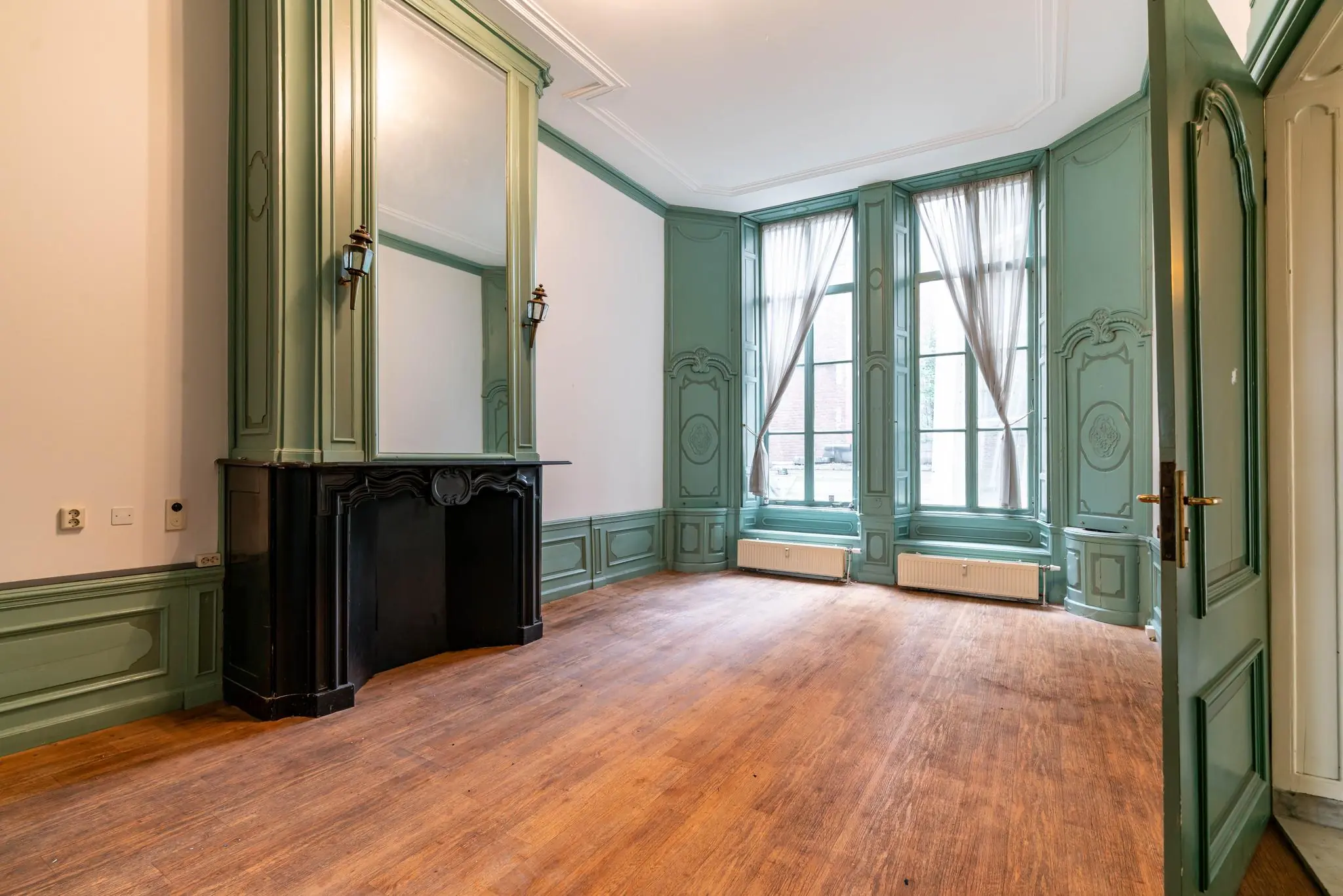 Klassieke kamer aan de Prinsengracht met hoge ramen, groene houten lambrisering en een sierlijke schouw.