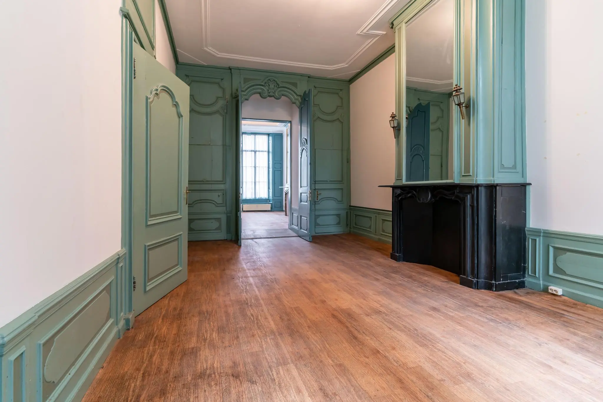 Klassieke kamer aan de Prinsegracht met houten vloer, hoge plafondlijsten en groen geschilderde wandpanelen en deuren.