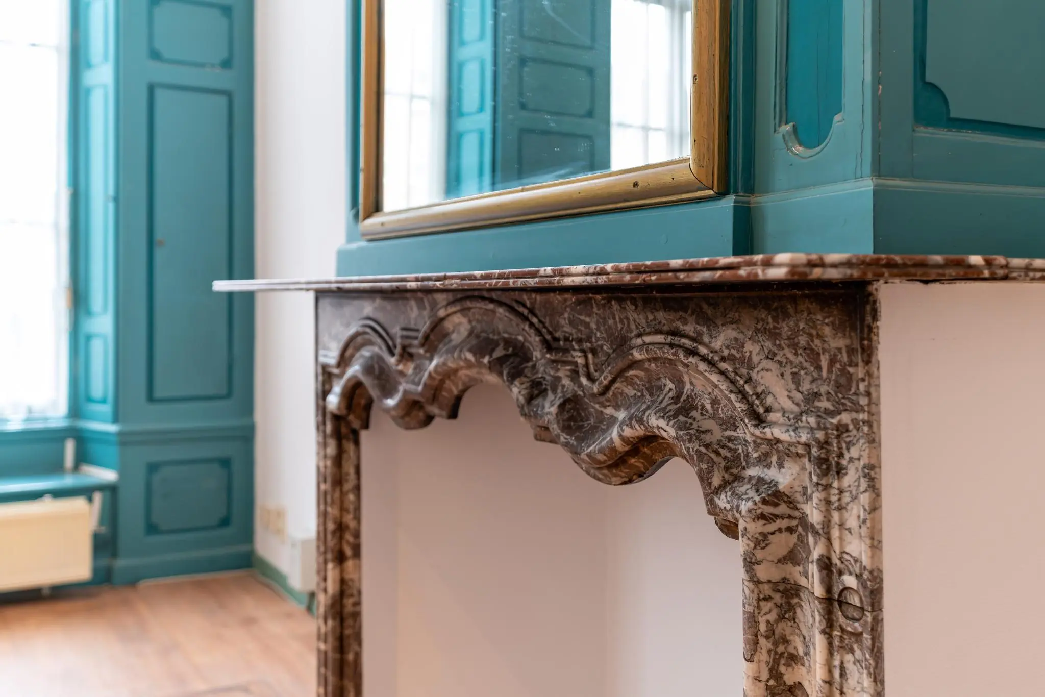 Close-up van een sierlijke marmeren schouw met blauwgroene houten lambrisering en een spiegel erboven in een historisch pand aan de Prinsegracht.