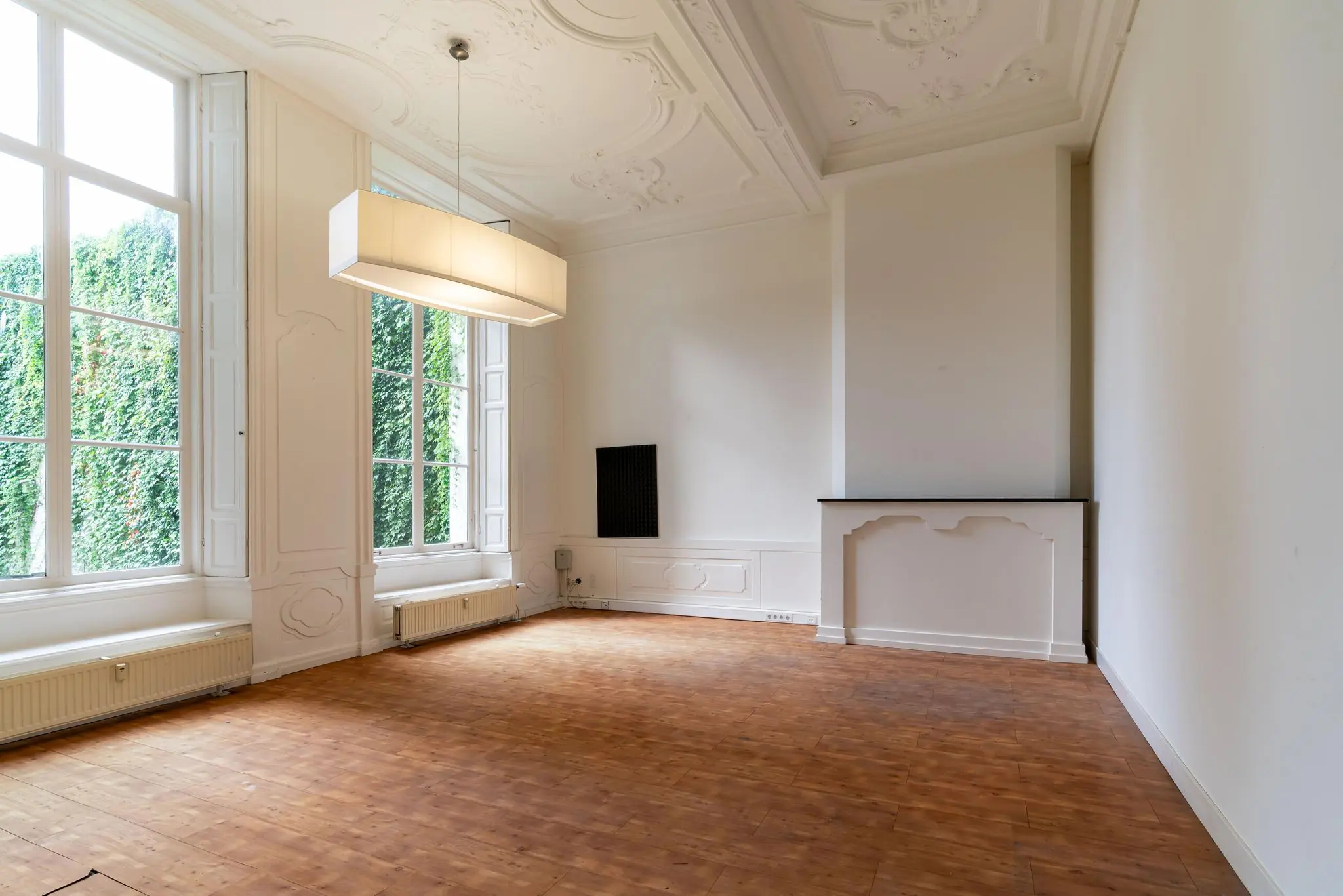 Lichte, lege kamer aan de Prinsegracht met hoge ramen, sierplafond en houten vloer.