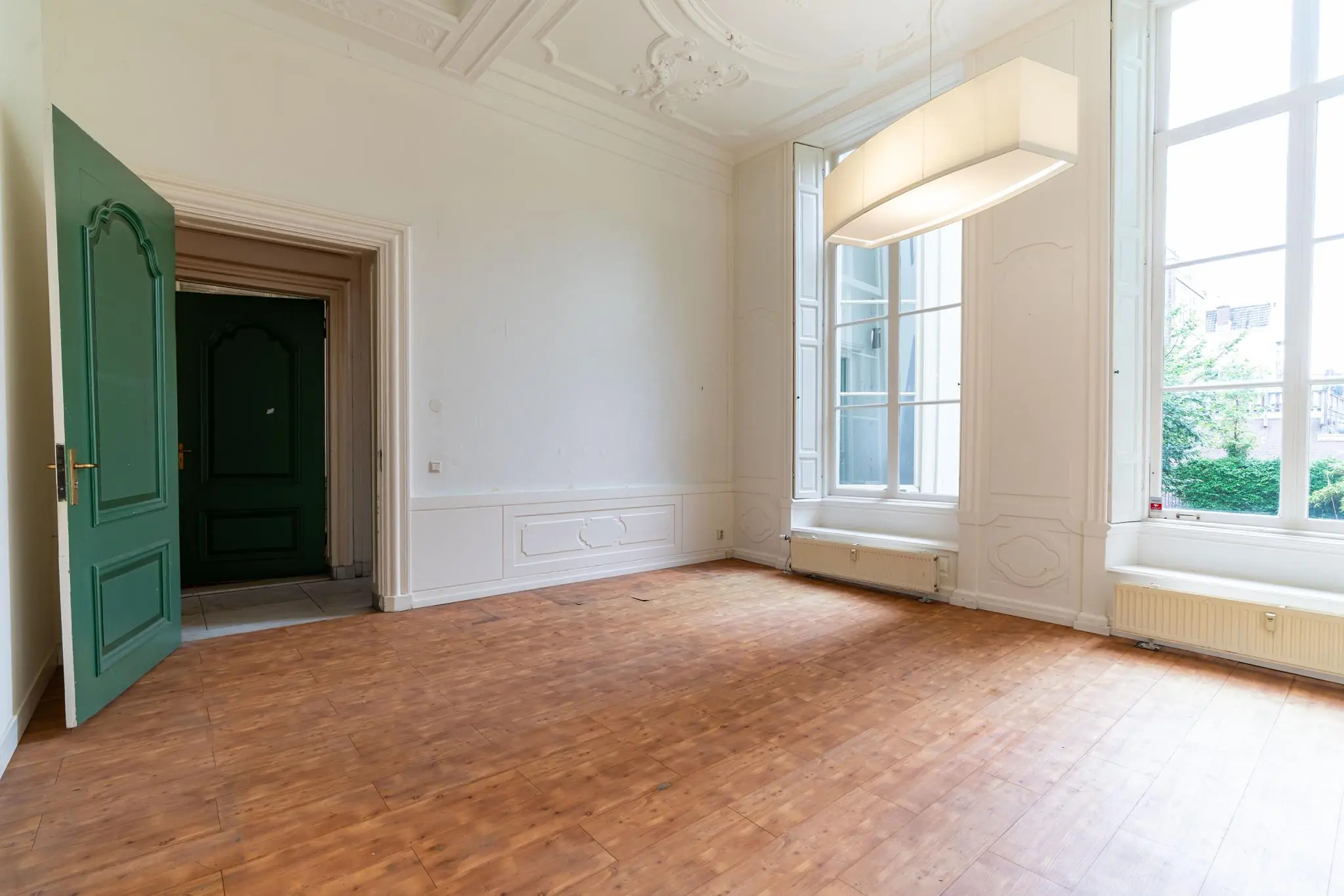 Lichte, hoge kamer aan de Prinsegracht met houten vloer, grote ramen en een groene deur.