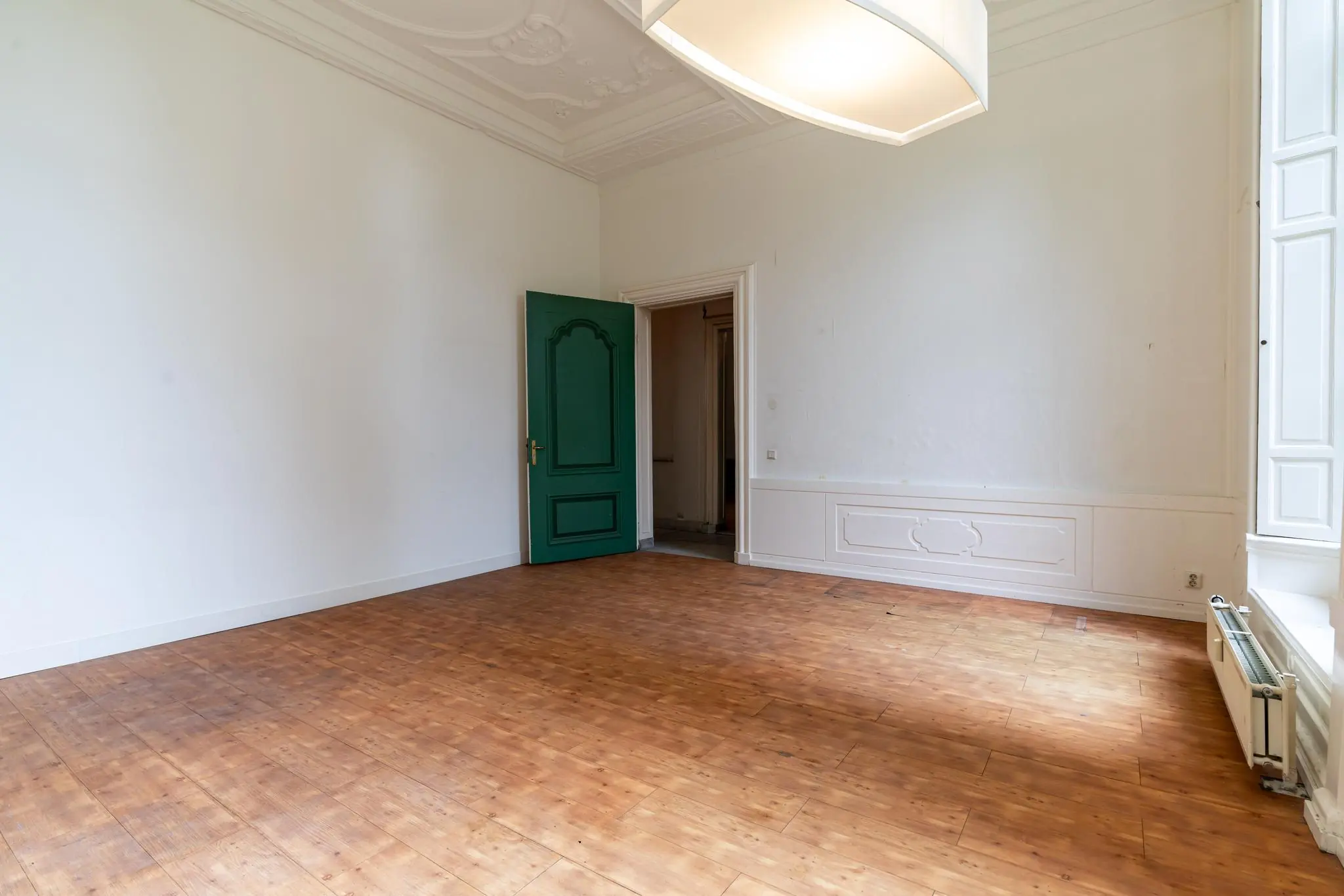 Lege kamer in een klassiek pand aan de Prinsegracht met houten vloer, witgesausde wanden en een groene deur.