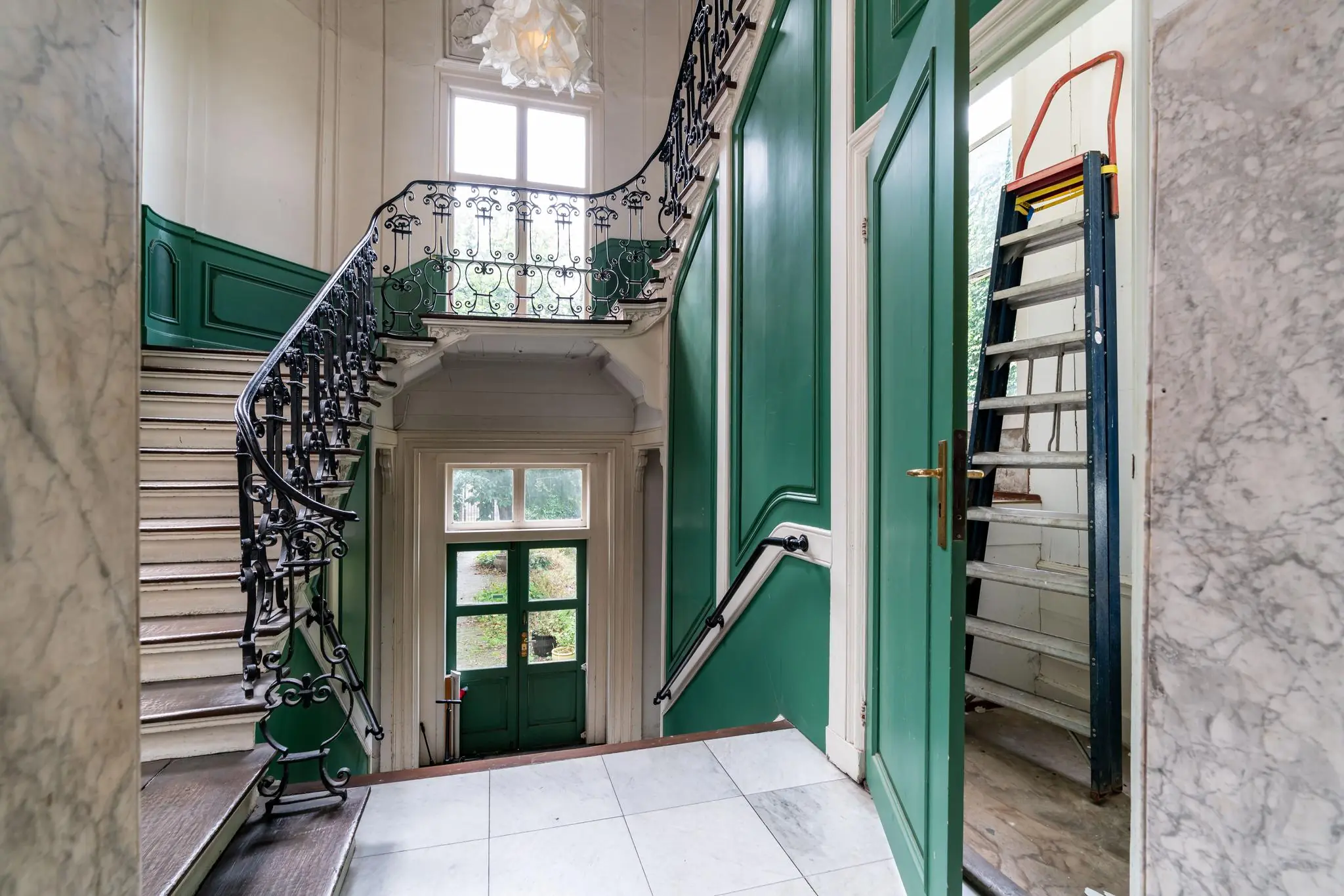 Monumentaal trappenhuis aan de Prinsegracht met sierlijk smeedijzeren hekwerk, groene deuren en een opklapbare ladder in een openstaande kastdeur.