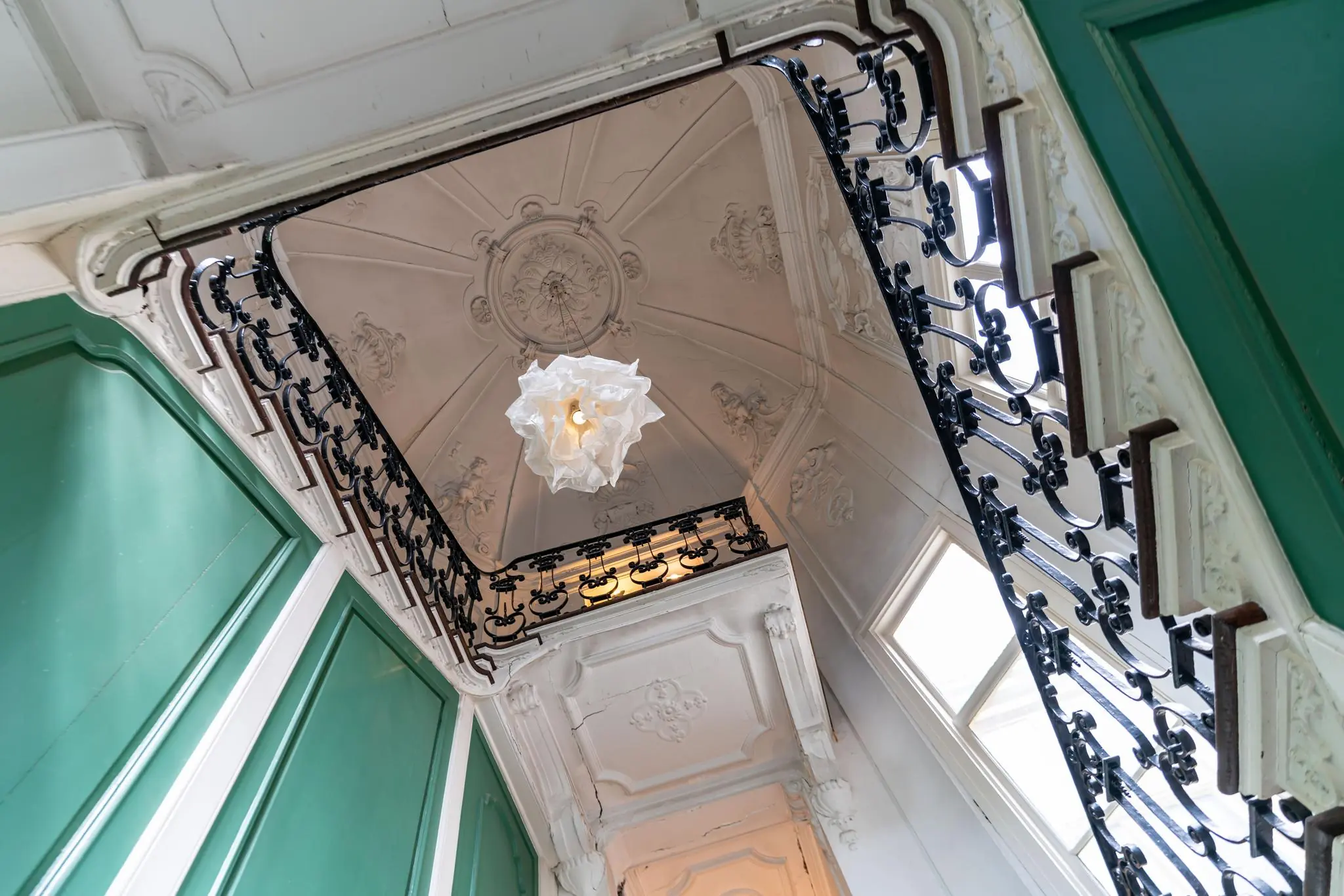 Trapportaal met sierlijk stucplafond, smeedijzeren trapleuning en groene paneeldeuren aan de Prinsegracht.