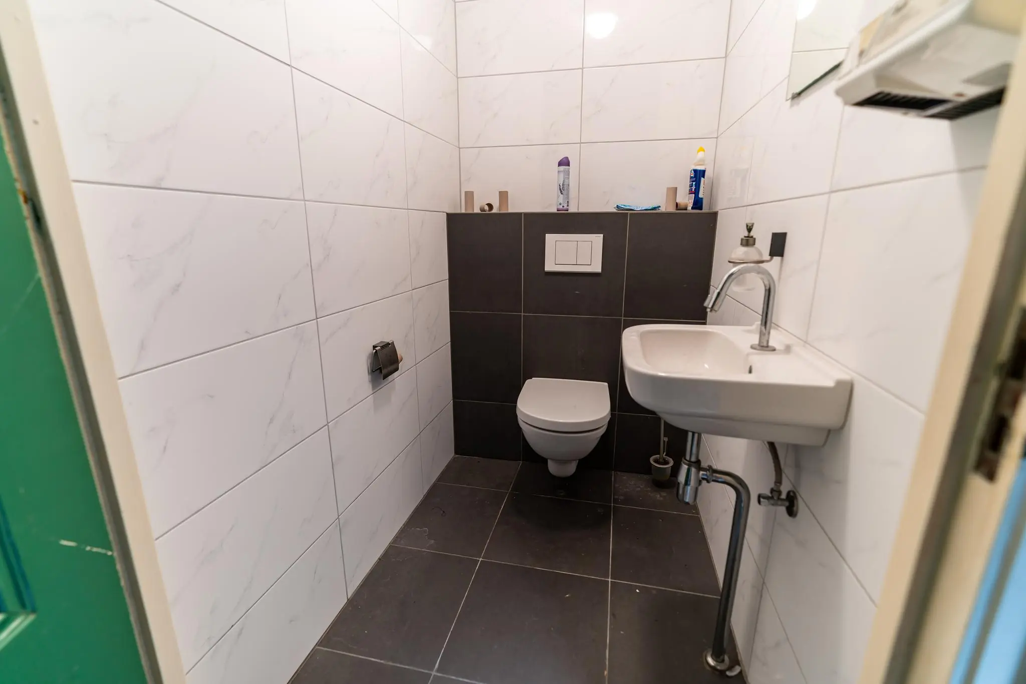 Moderne toiletruimte aan de Prinsegracht met wit-zwarte betegeling, wandcloset en een kleine wastafel.