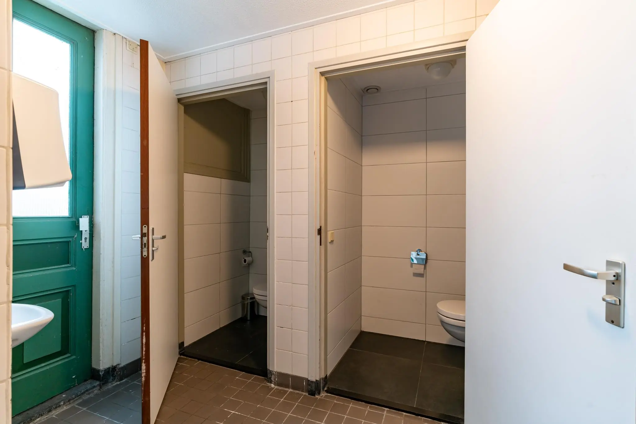 Twee aparte toiletruimtes met witte betegeling en openstaande deuren in een gedeelde sanitaire ruimte aan de Prinsegracht.