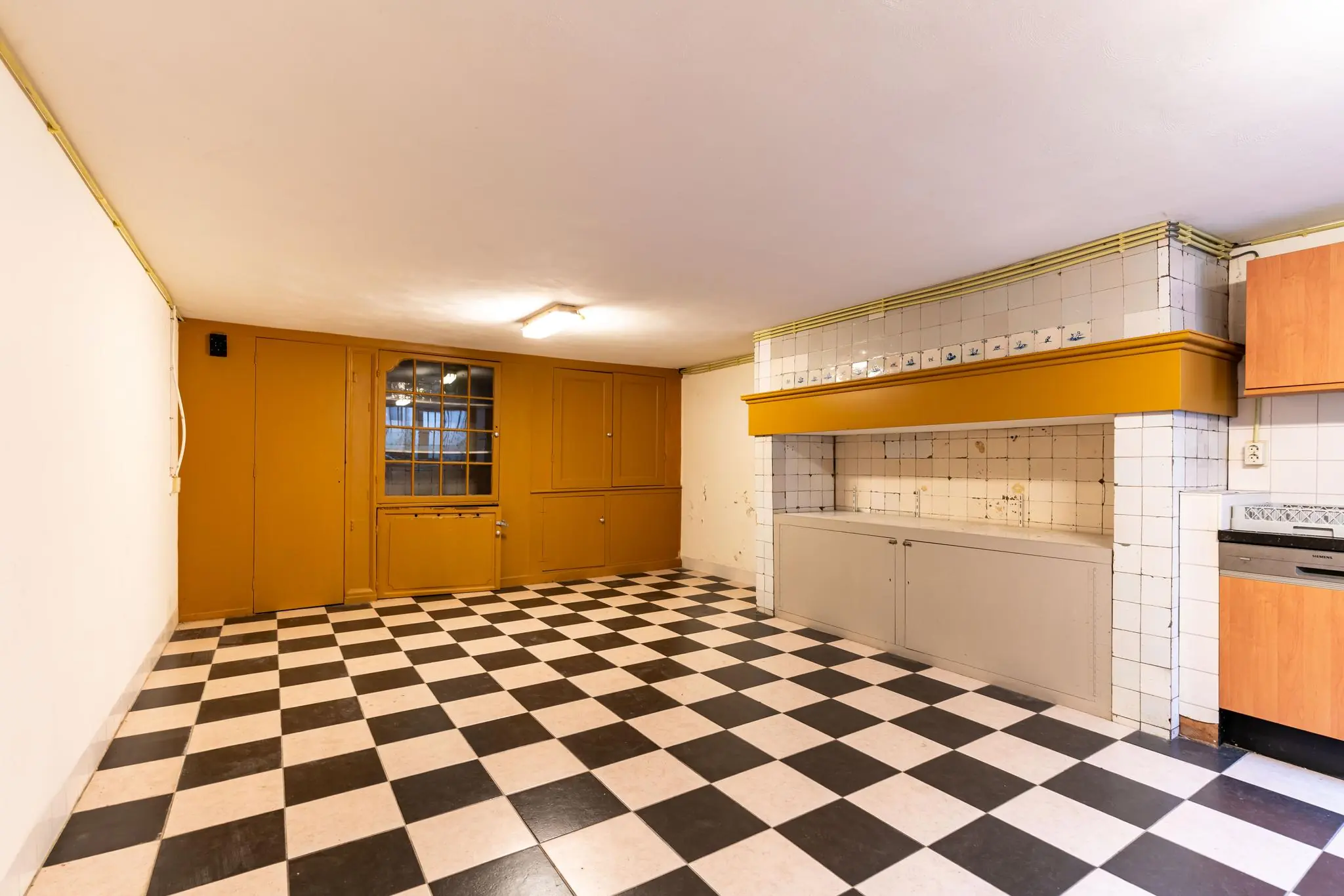 Keukenruimte aan de Prinsegracht met zwart-wit geblokte vloer, mosterdgele accenten en betegelde schouw.