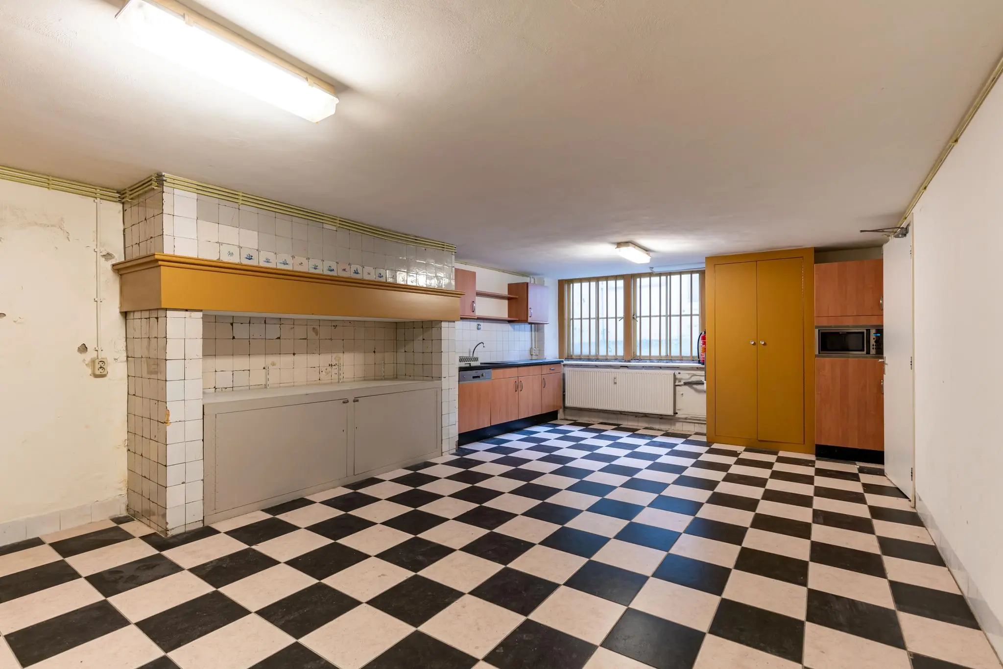 Keuken met zwart-wit geblokte tegelvloer, houten kastjes en betegelde schouw aan de Prinsegracht.