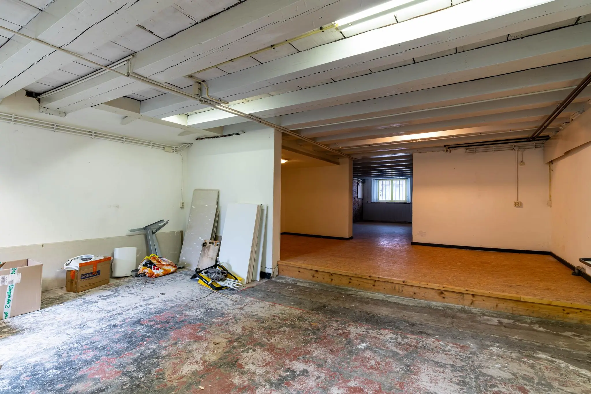 Ongerenoveerde ruimte in een souterrain aan de Prinsegracht met houten plafondbalken en bouwmaterialen op de vloer.