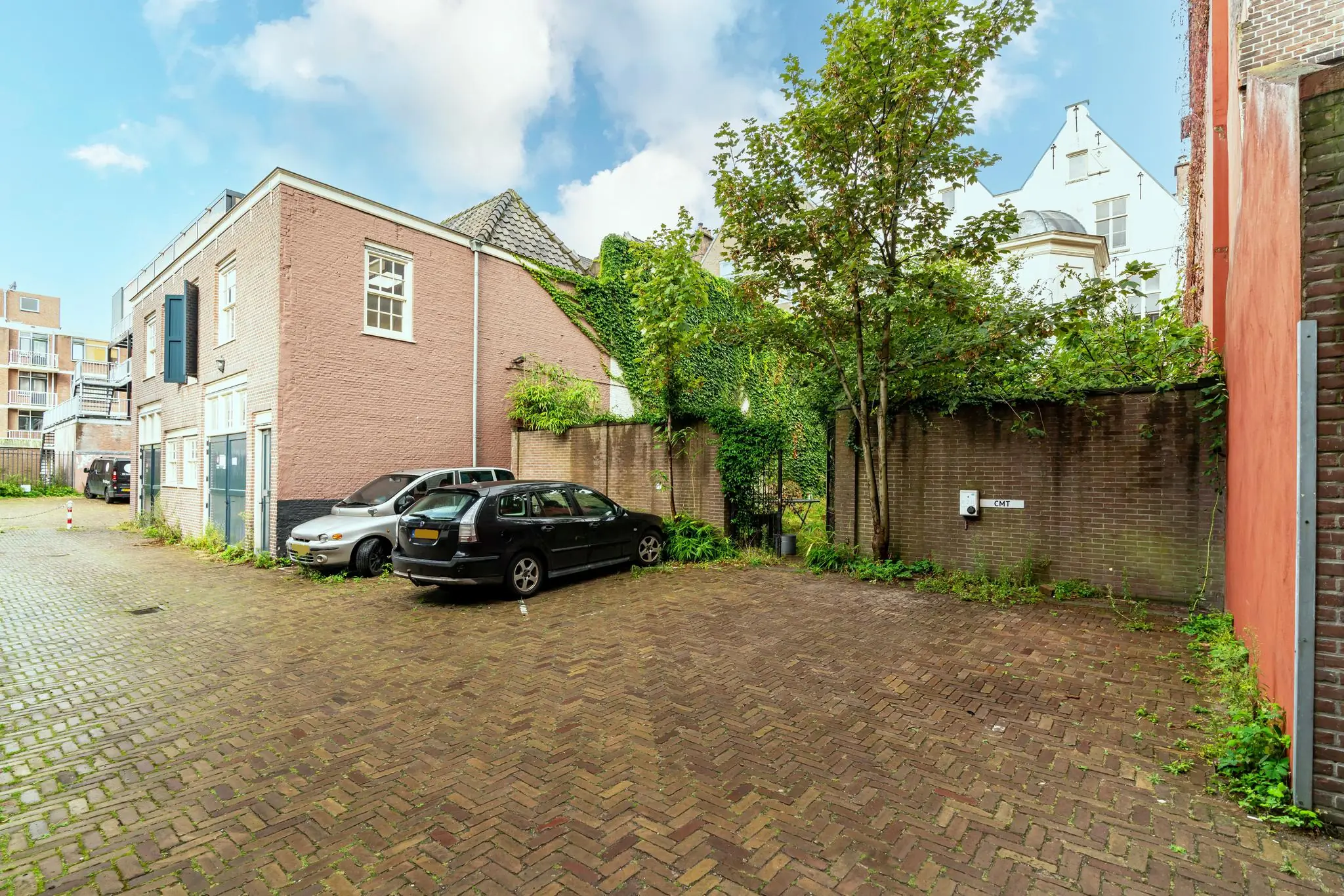 Bestrate parkeerplaats aan de Prinsegracht met geparkeerde auto's naast historische bebouwing en groene gevelbegroeiing.