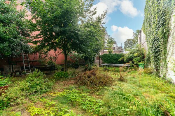 Begroeide stadstuin aan de Prinsegracht met bomen, tuinmeubilair, een trampoline en een muur begroeid met klimop.