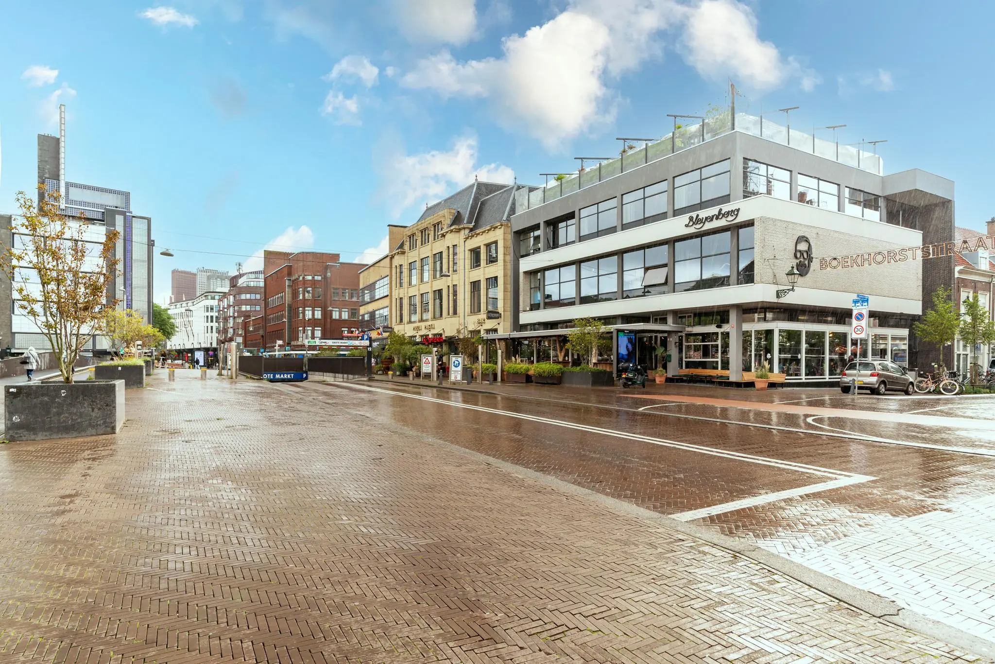 Straatbeeld van de Prinsegracht in Den Haag met natgeregend plein, het restaurant Bleyenberg en de ingang van de Grote Markt tram- en metrohalte.