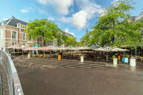 Terras met parasols en lege tafels aan de Prinsegracht in Den Haag op een zonnige dag.