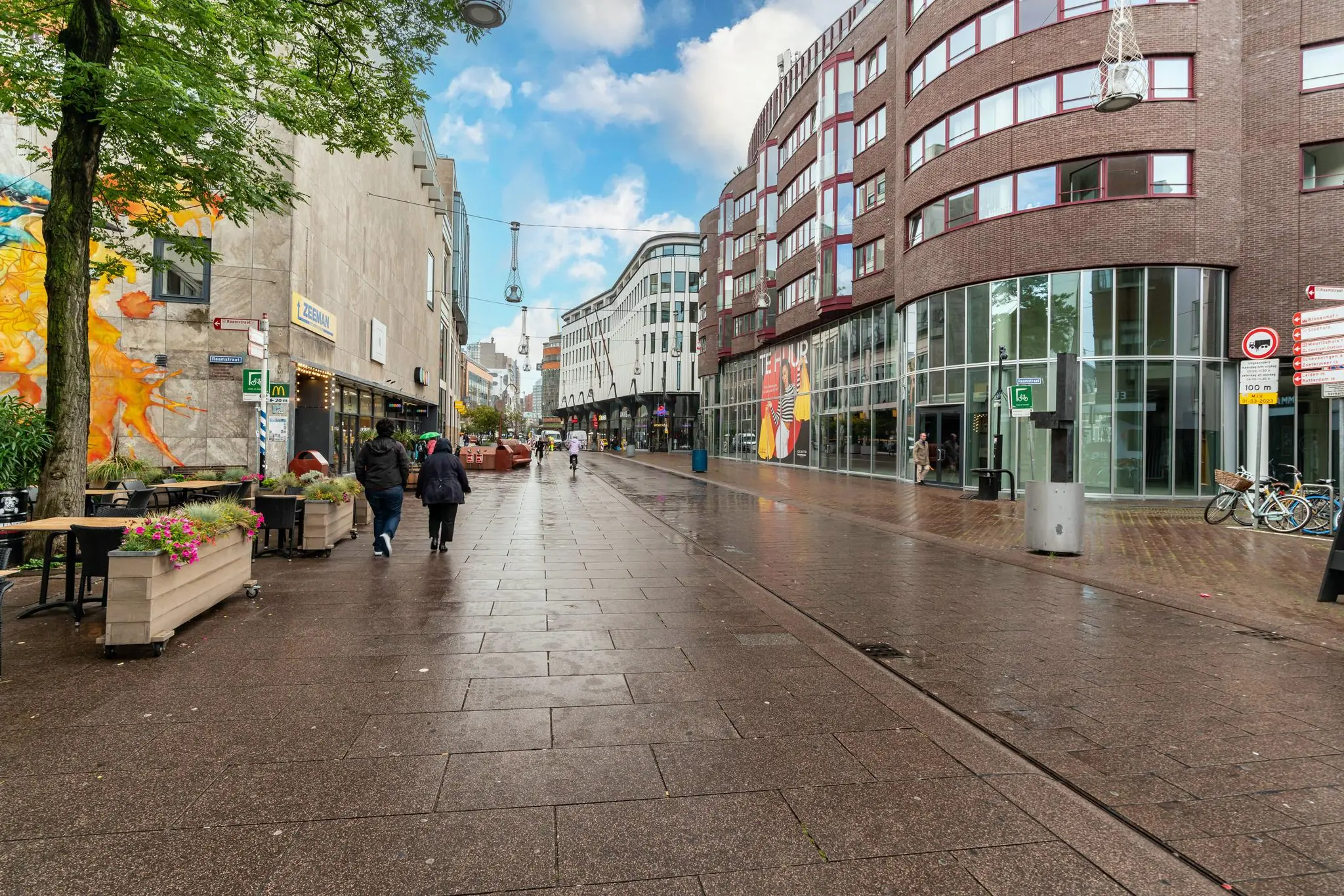 Winkelstraat Prinsegracht in Den Haag met moderne gebouwen, wandkunst en voorbijgangers op een natgeregend trottoir.